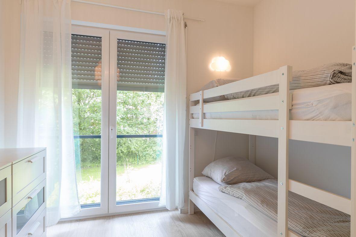 Zimmer mit Doppelstockbett, Schrank und Fenster zur grünen Außenseite.