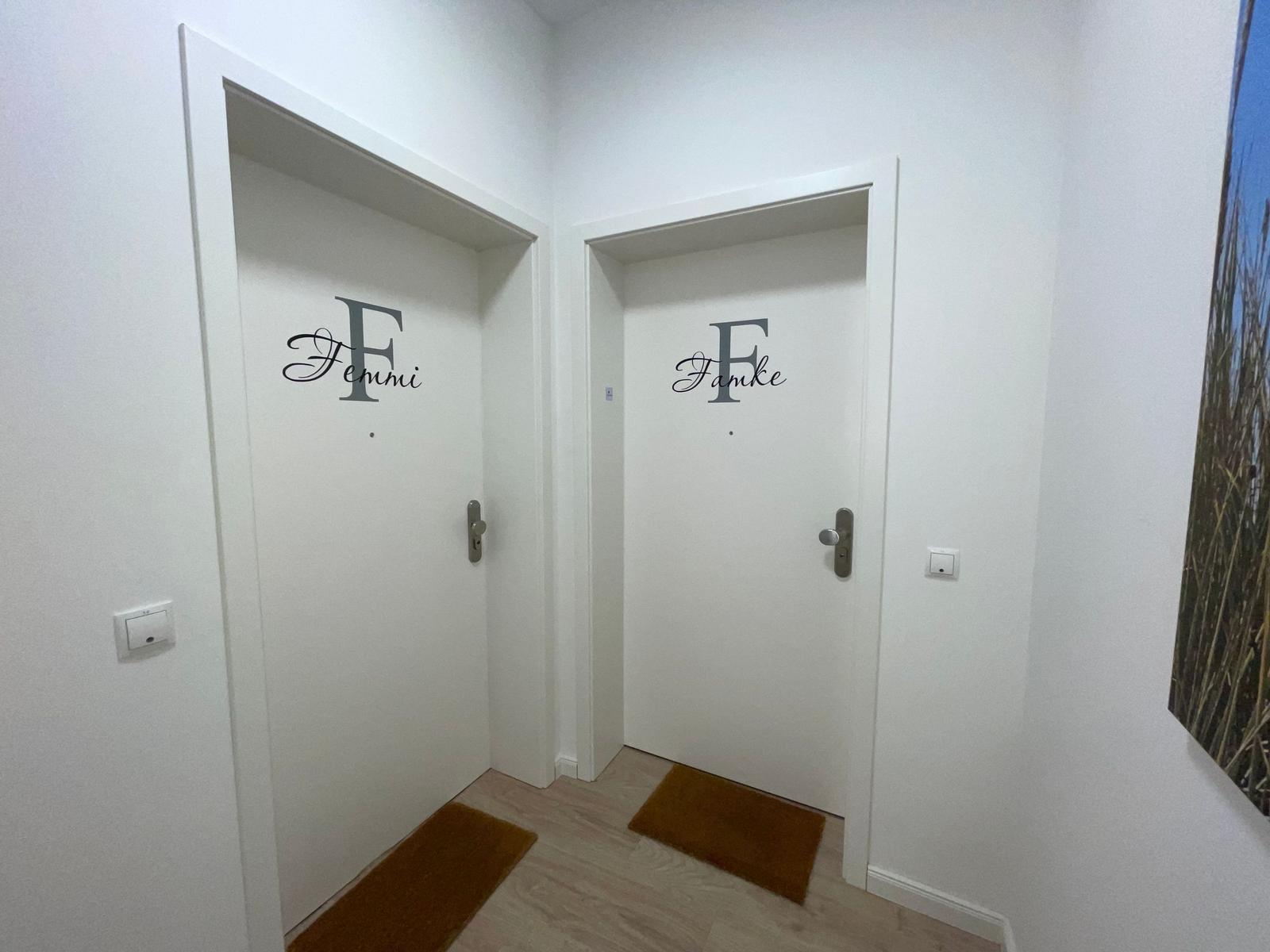 Tür mit Aufschrift Femmi in einem Flur mit Holzboden und Wandbildern