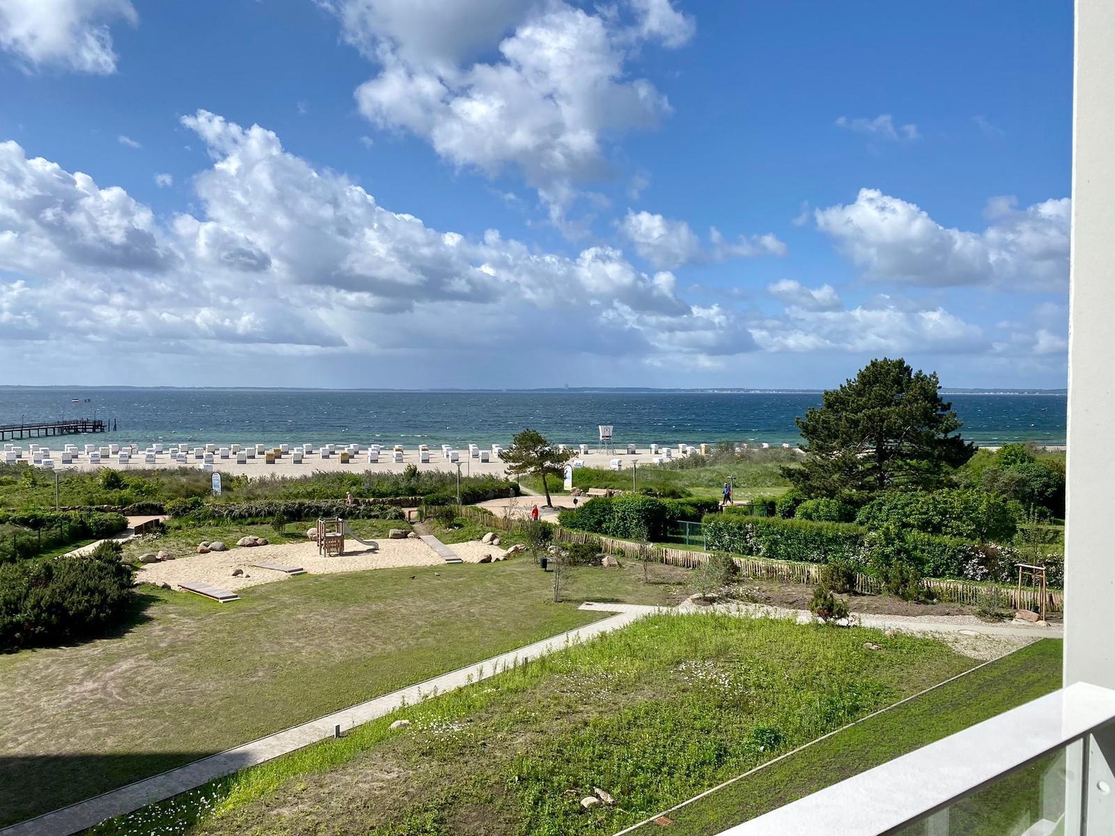 Strand mit Steg, Strandkörben und Meer unter bewölktem Himmel