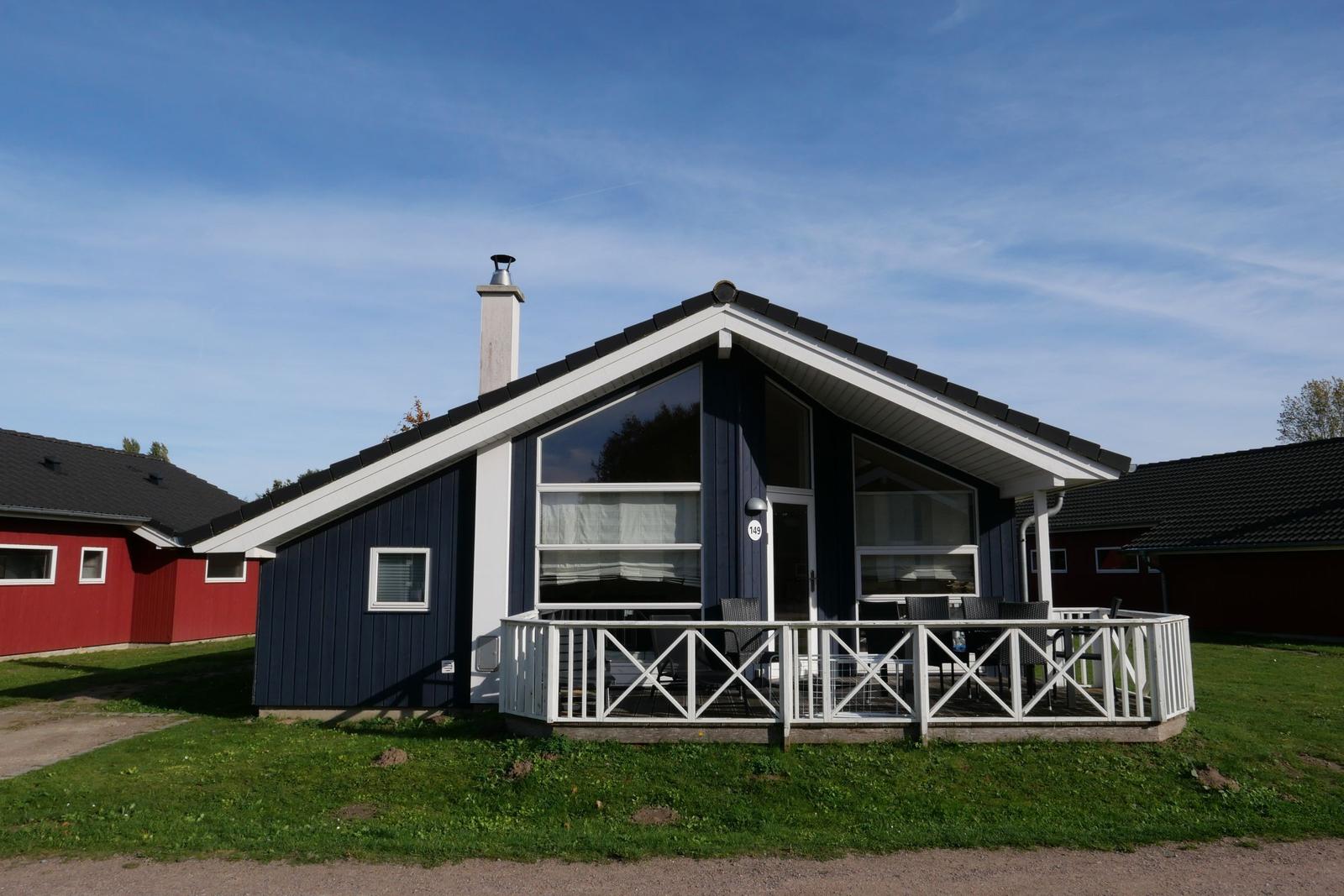 Blau gestrichenes Haus mit Terrasse und Fenstern. Grasfläche und klare Himmel.