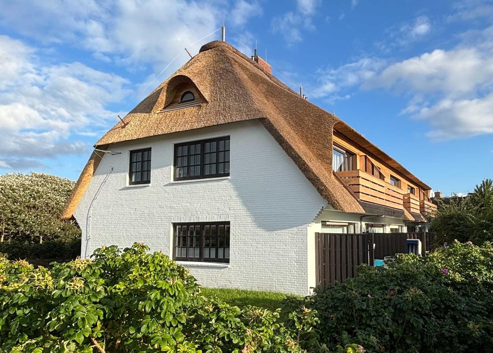 Terrasse mit Gartenmöbeln und Blick auf Haus mit Strohdach.