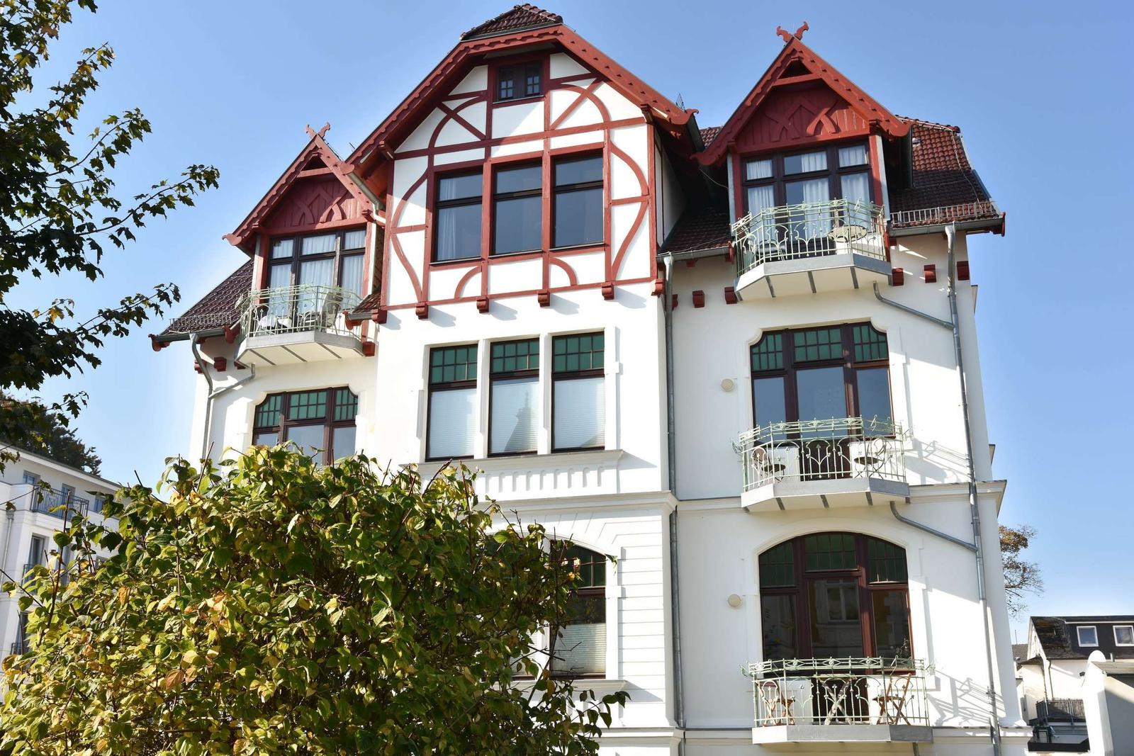 Haus mit weißen Wänden und roten Dachdetails. Mehrere Balkone mit Metallgeländern.