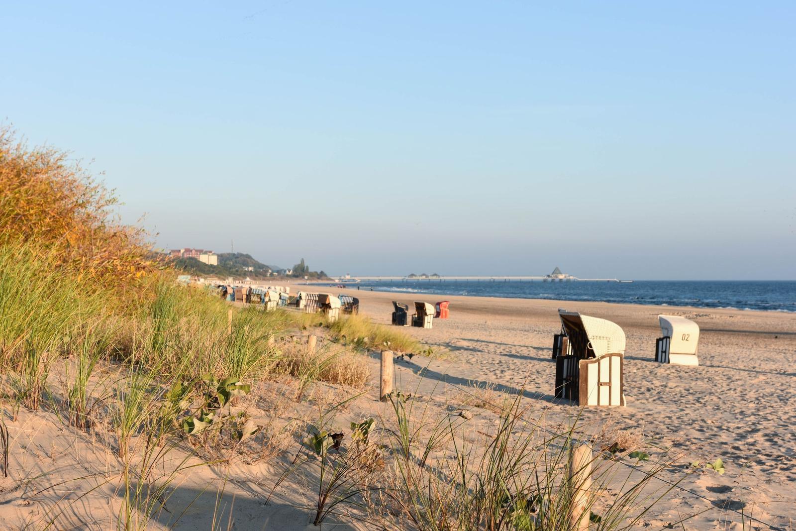 Strandhütte mit Terrasse, roten Sonnenschirmen und Flaggen an klarem Himmel.