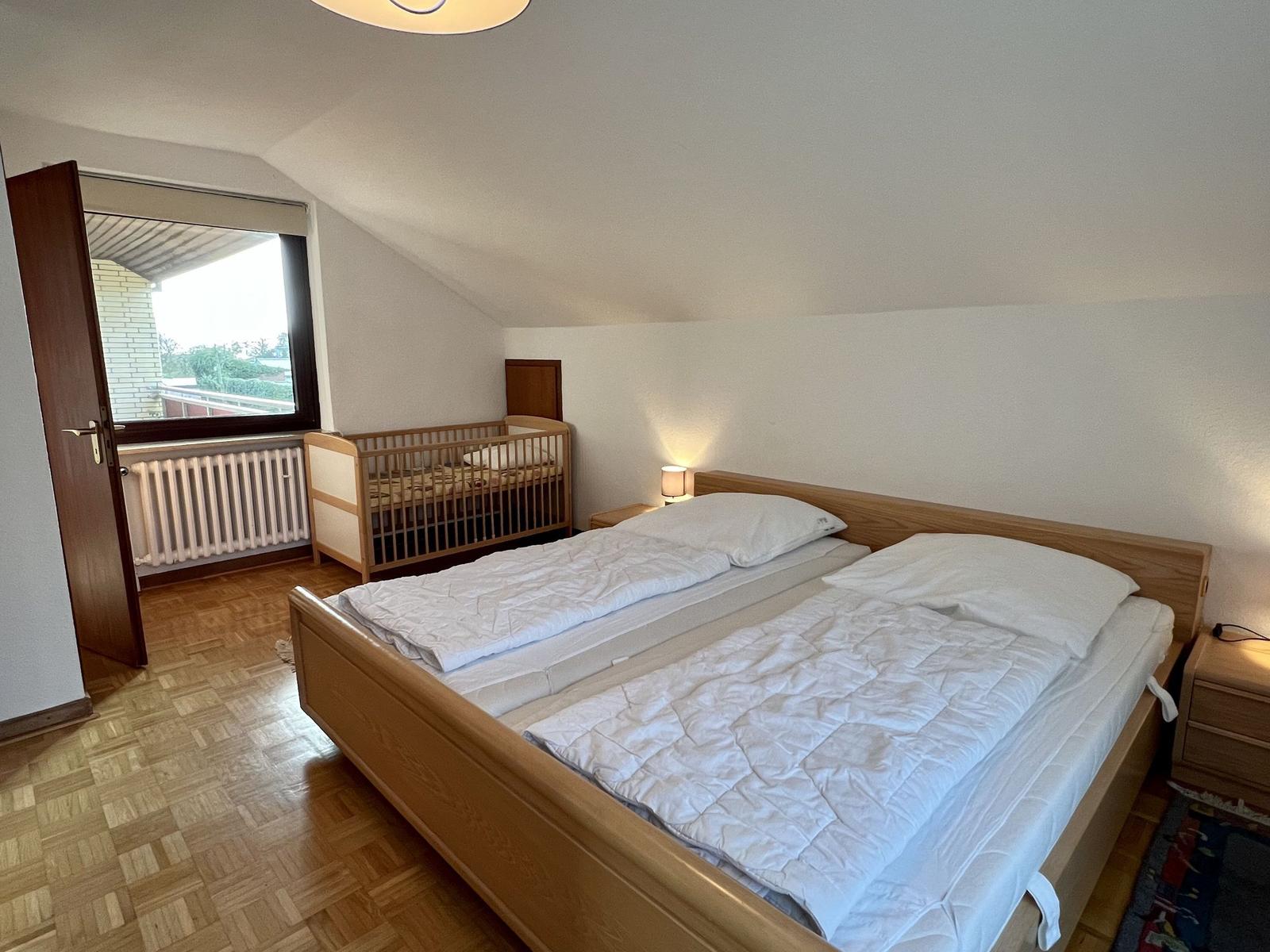 Schlafzimmer mit Doppelbett, Spiegelschrank und Fenster mit Jalousie.
