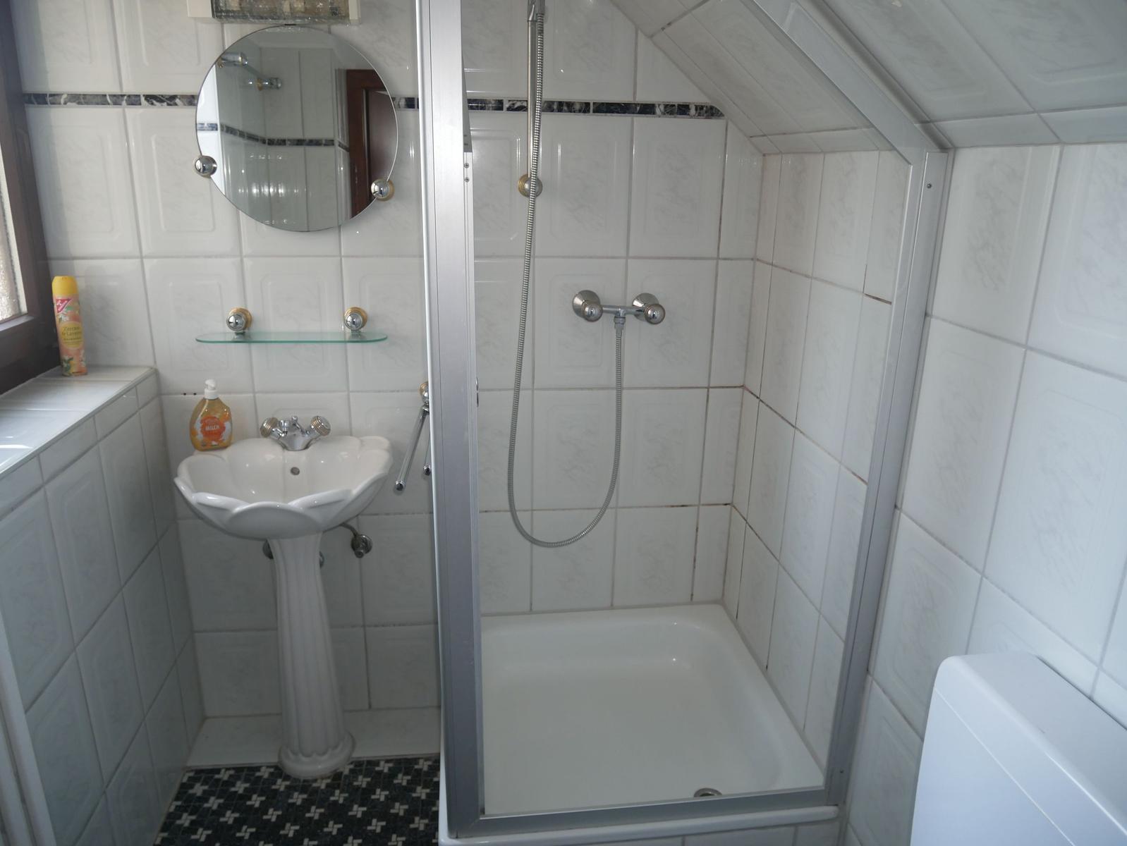 Schlafzimmer mit Doppelbett, zwei Stühlen und Holzboden. Fenster mit Vorhängen.