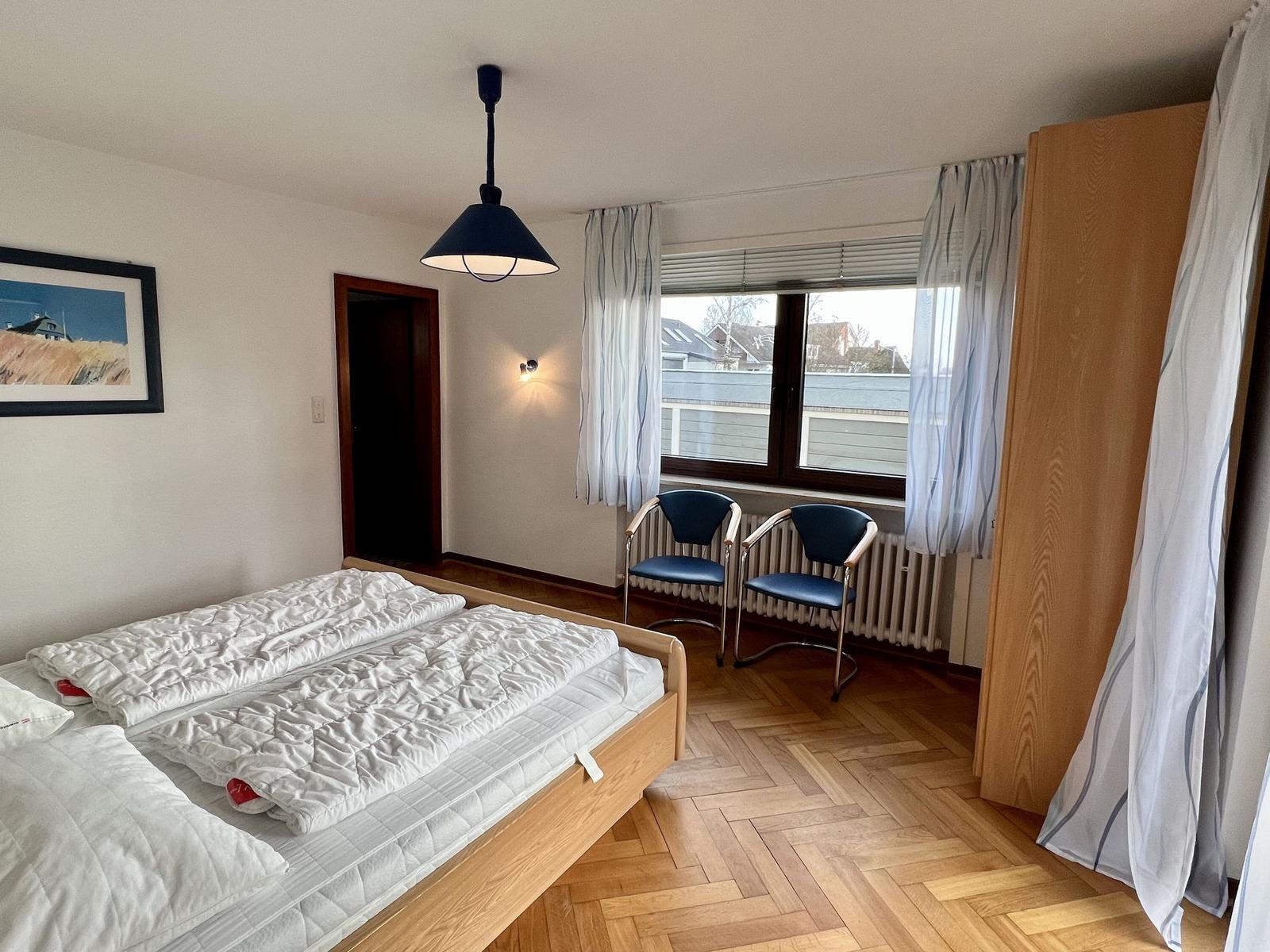 Schlafzimmer mit Doppelbett, Fenster, TV und Teppichboden.