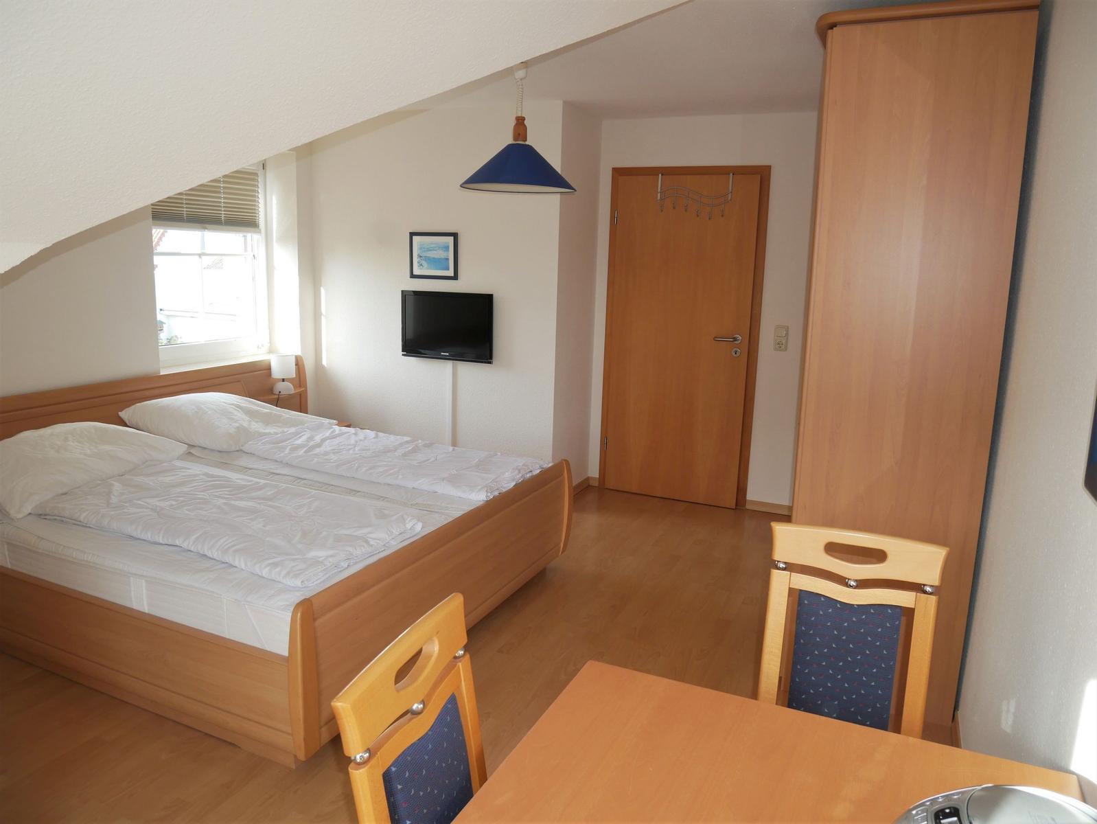 Schlafzimmer mit Bett, Kleiderschrank und Fenster mit Blick auf Dach.