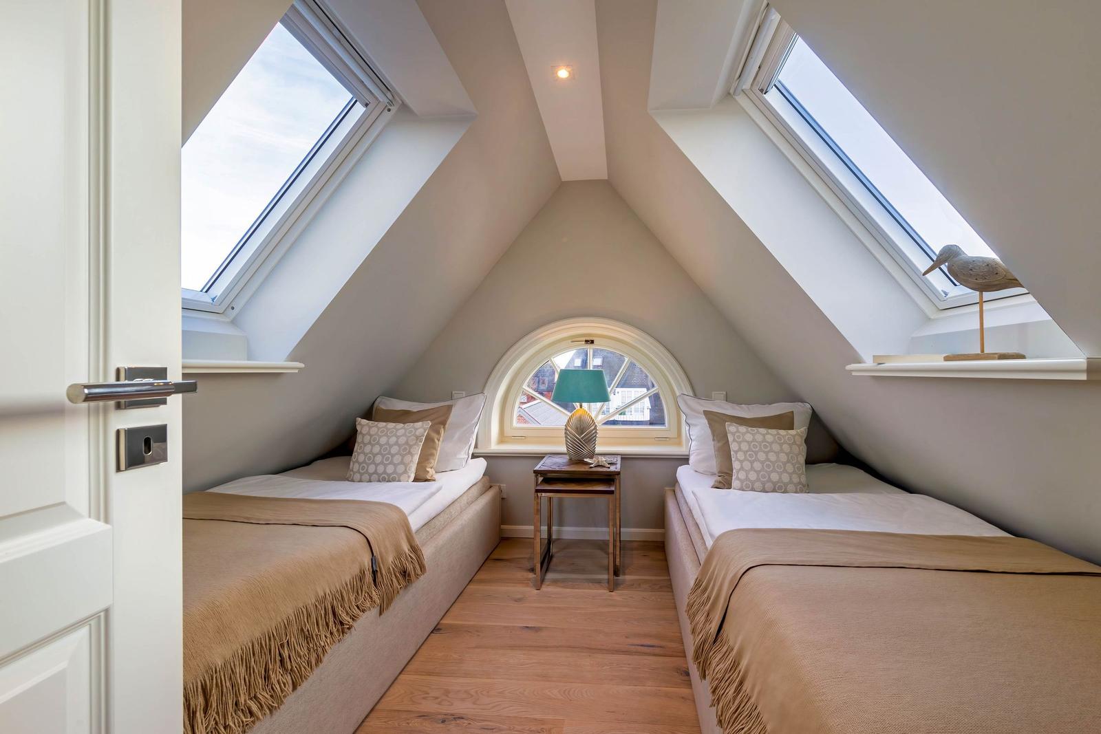 Zimmer mit zwei Betten, Dachschrägen und Dachfenster mit Vogeldekoration.