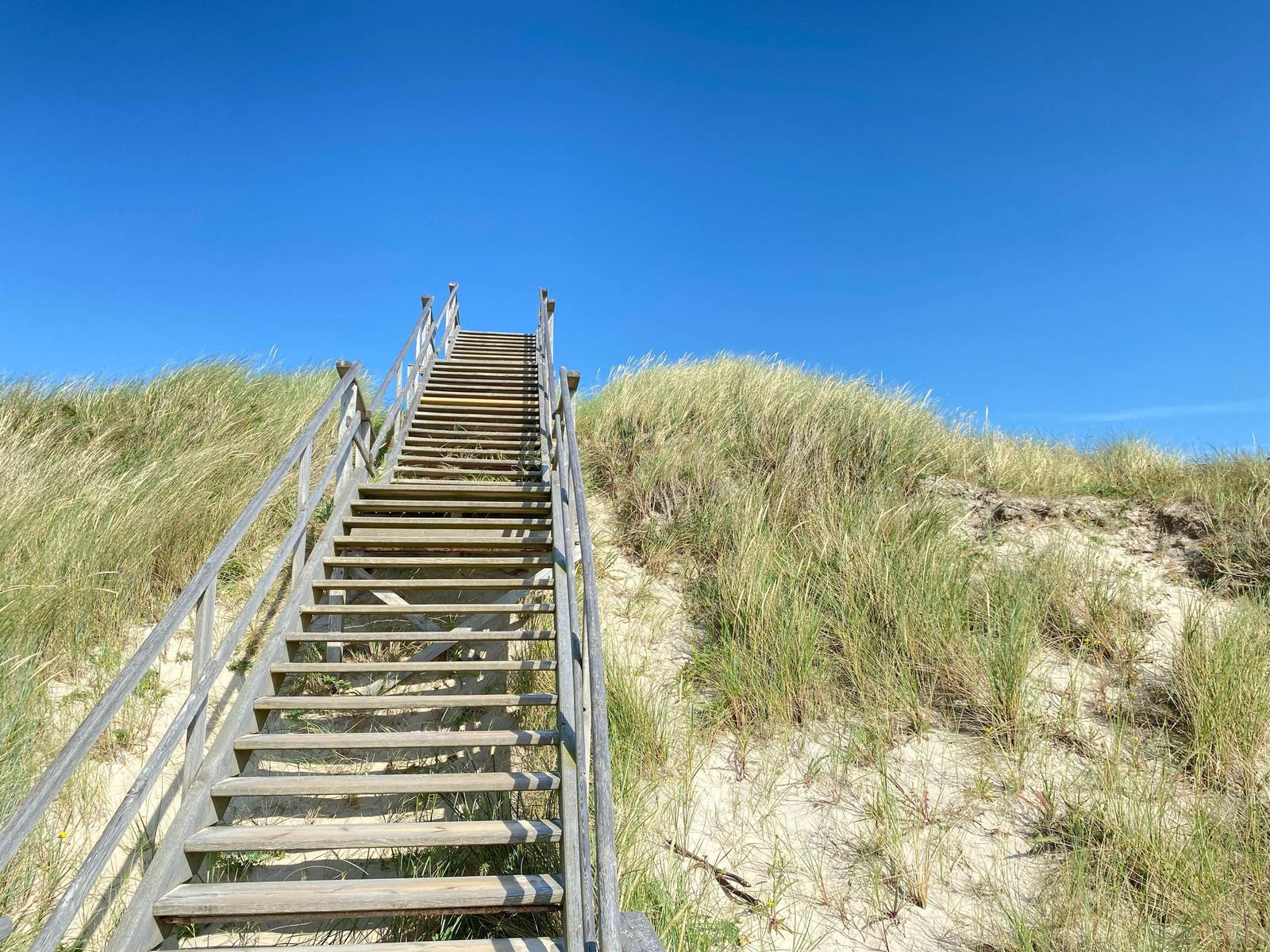 Strand mit Sanddünen und Strandkörben unter blauem Himmel.