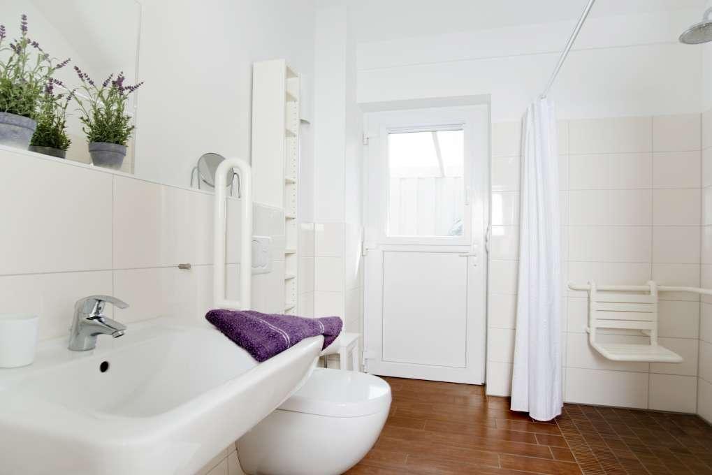 Badezimmer mit Waschbecken, WC und Handtuchhalter. Weiße Fliesen und Pflanze.