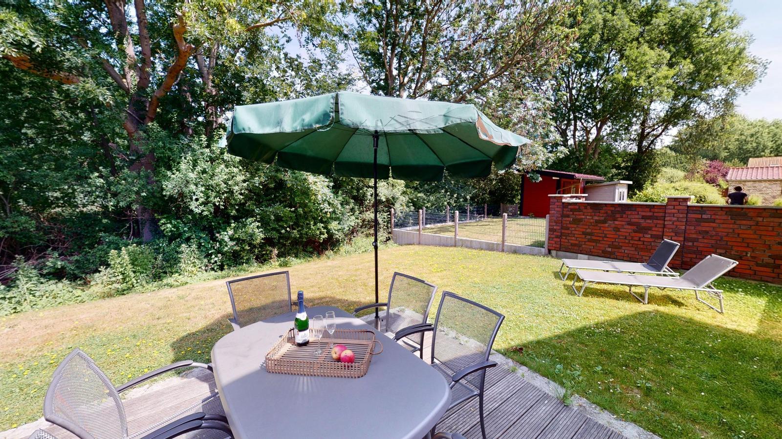 Terrasse mit Tisch, sechs Stühlen und Liegestuhl mit Streifen.