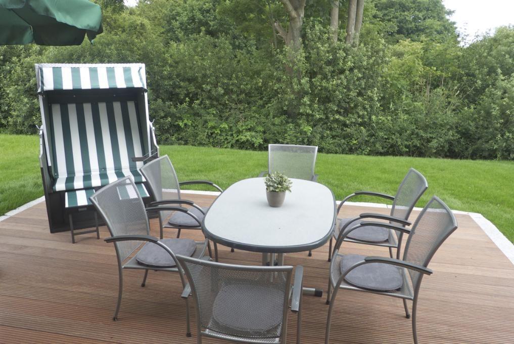 Haus mit Terrasse, grünem Sonnenschirm und Liegestuhl im Garten.