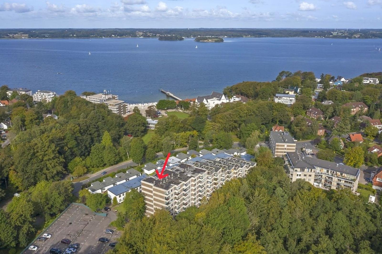 Aerial view of a coastal area with buildings, forest, and water.