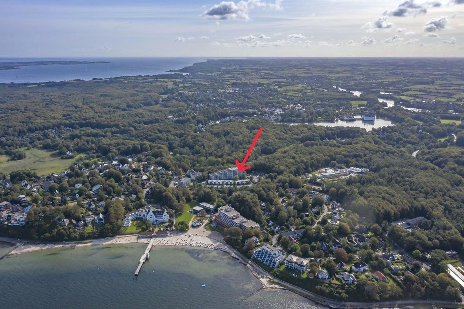Strand mit Steg, Liegestühlen und Booten im Hintergrund.