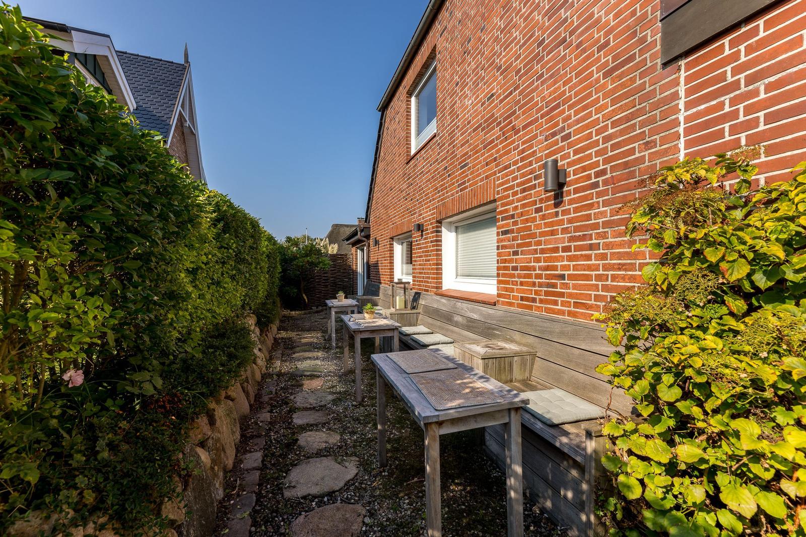 Terrasse mit Holztisch, Bank und Pflanzen an rotem Ziegelhaus