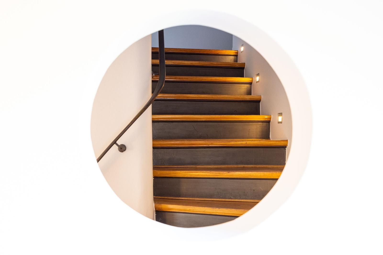 Flur mit Holzboden, Wandlampen und Bild. Treppe mit Holzstufe und Metallgeländer.