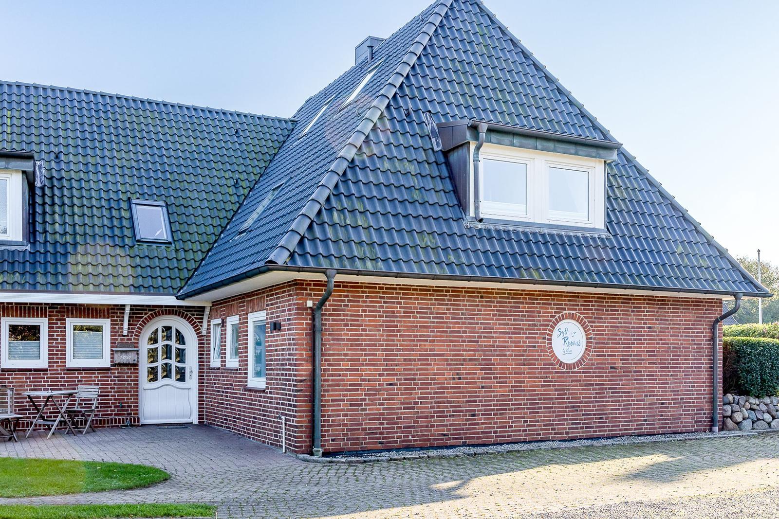 Haus mit Steinmauer, weißen Türen und Schild Sylt Rooms.