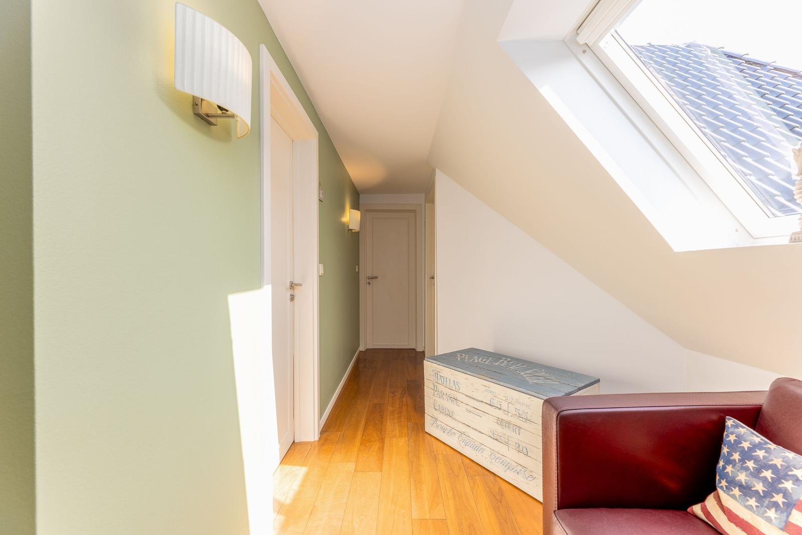 Dachgeschosszimmer mit Holzboden, Dachschrägen, Fenster und Sitzgelegenheit.