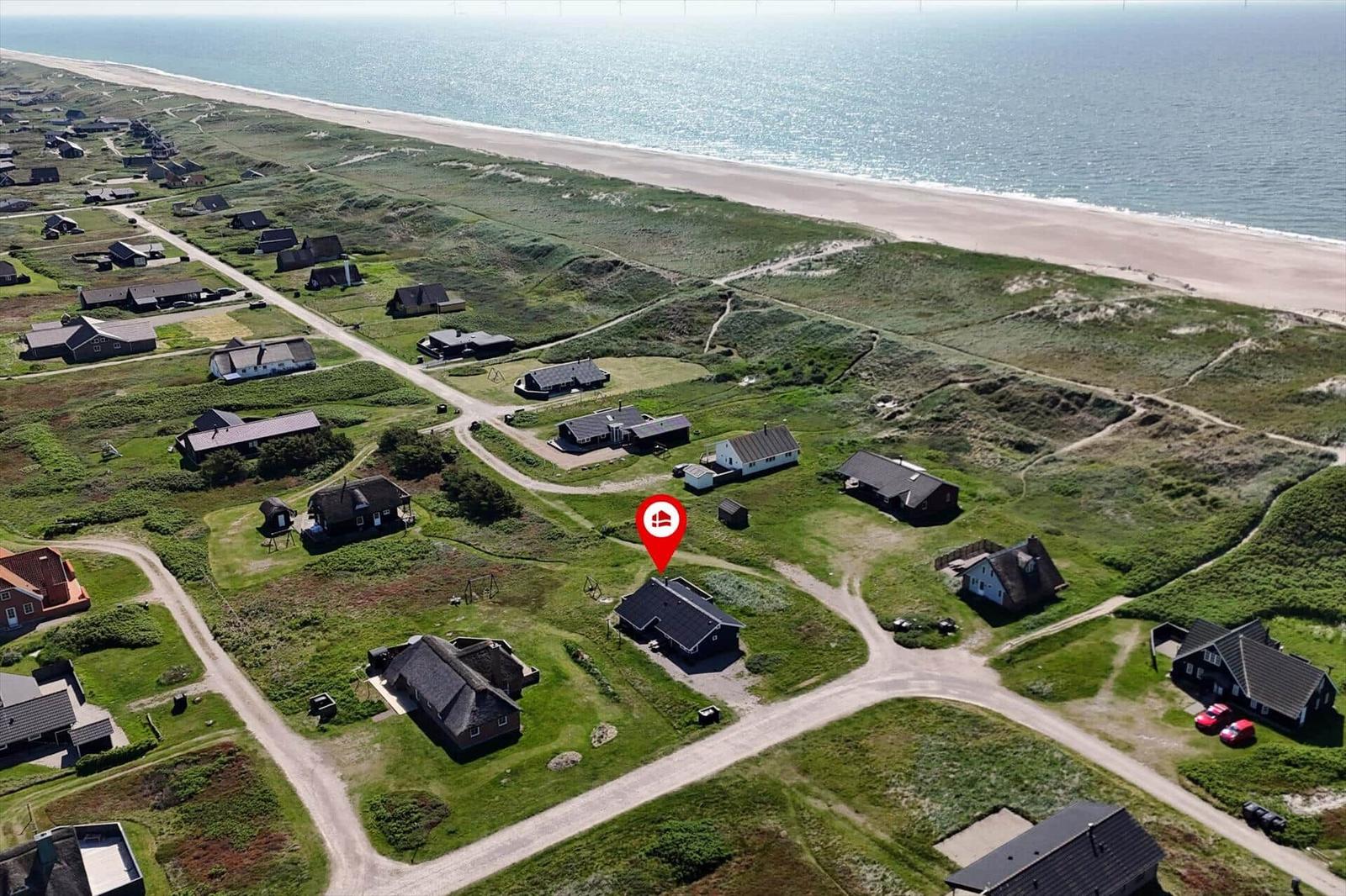 Haus mit rotem Markierungspunkt in Strandnähe, umgeben von Grünflächen und weiteren Häusern.