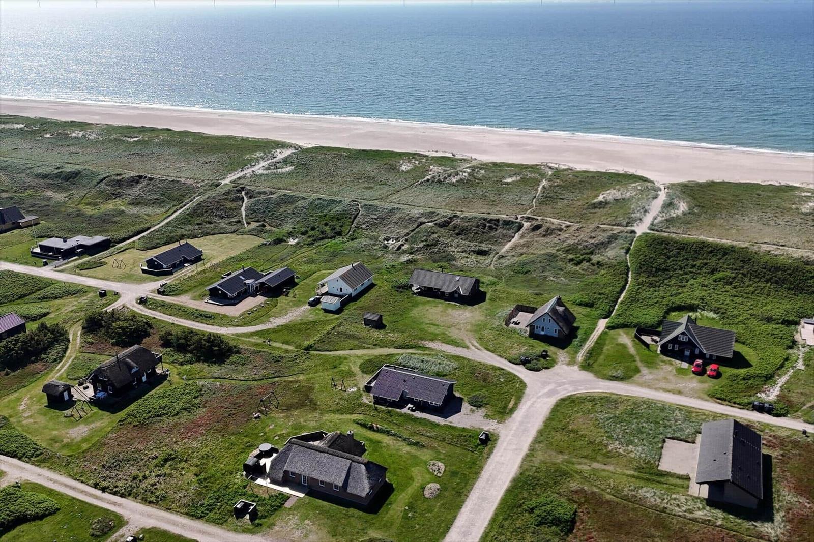Aerial view of coastal houses with sandy beach and dunes.