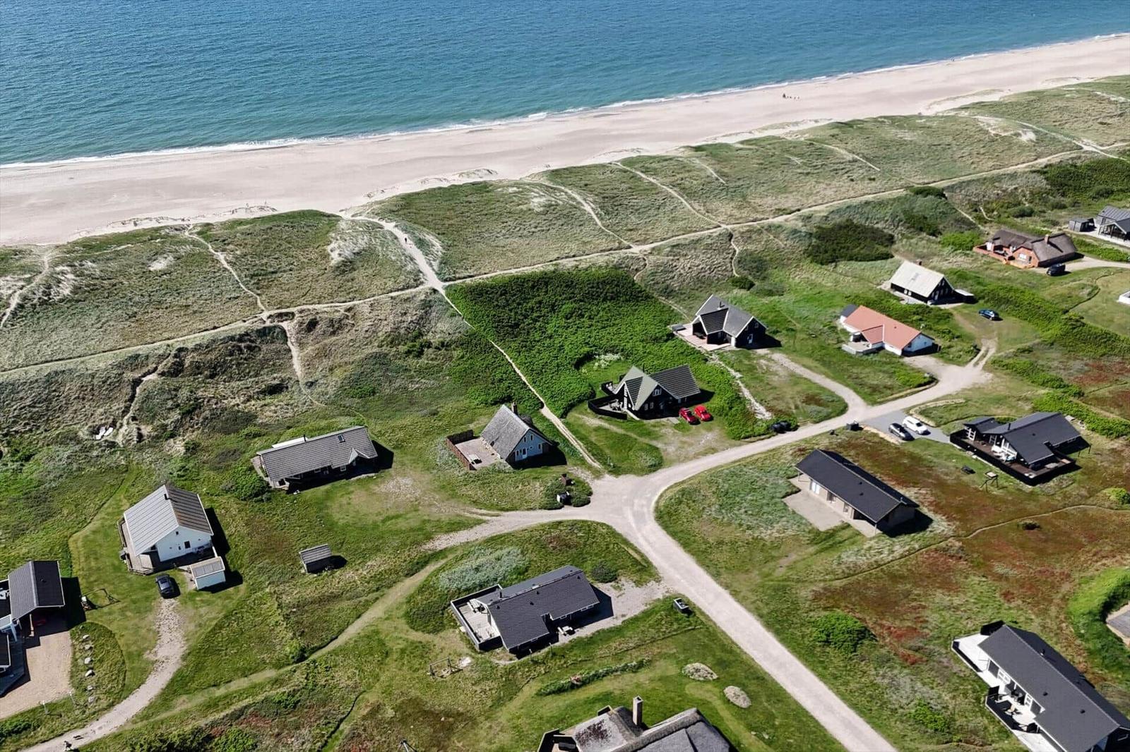 Aerial view of beachside houses on green dunes near the sea.