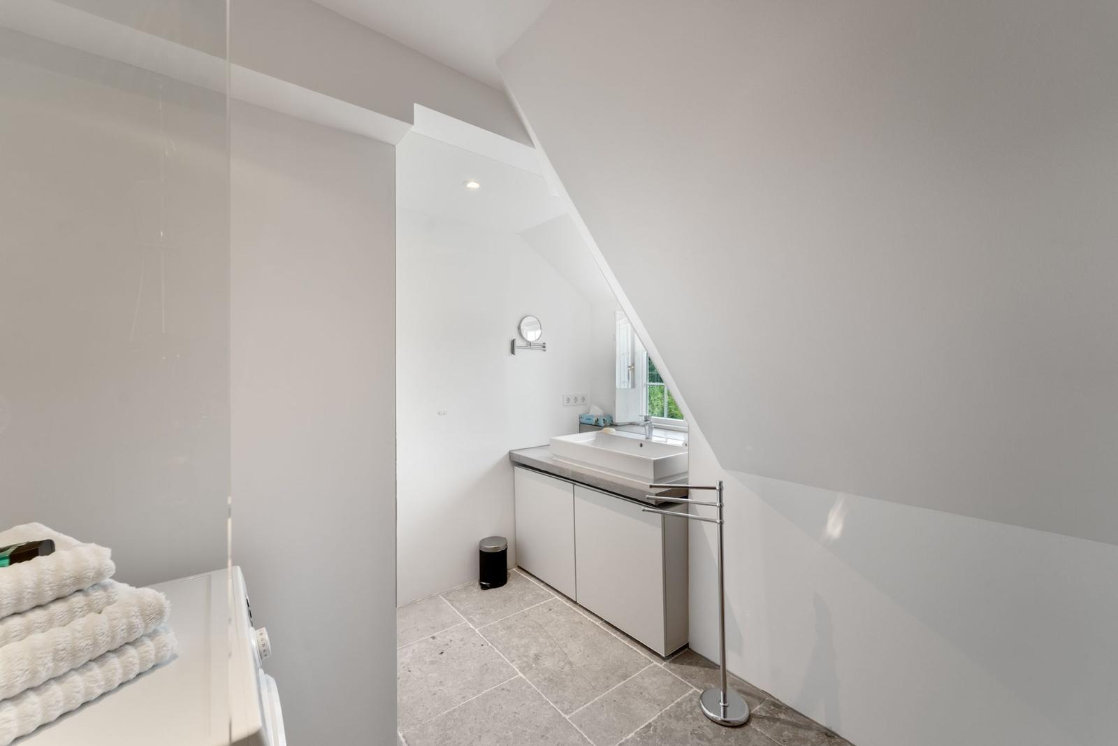 Dusche mit Glaswand, Toilette und Waschmaschine in weißer Umgebung.