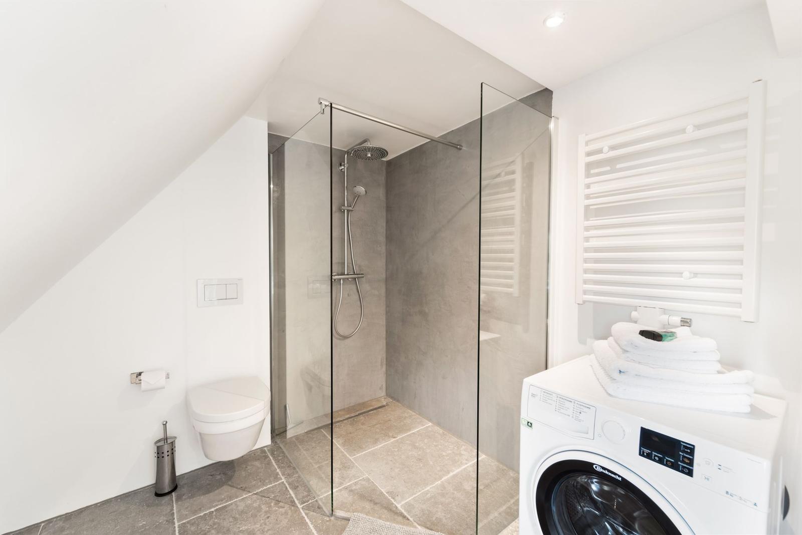 Badezimmer mit Dusche, Toilette und Waschmaschine unter Dachschrägen.