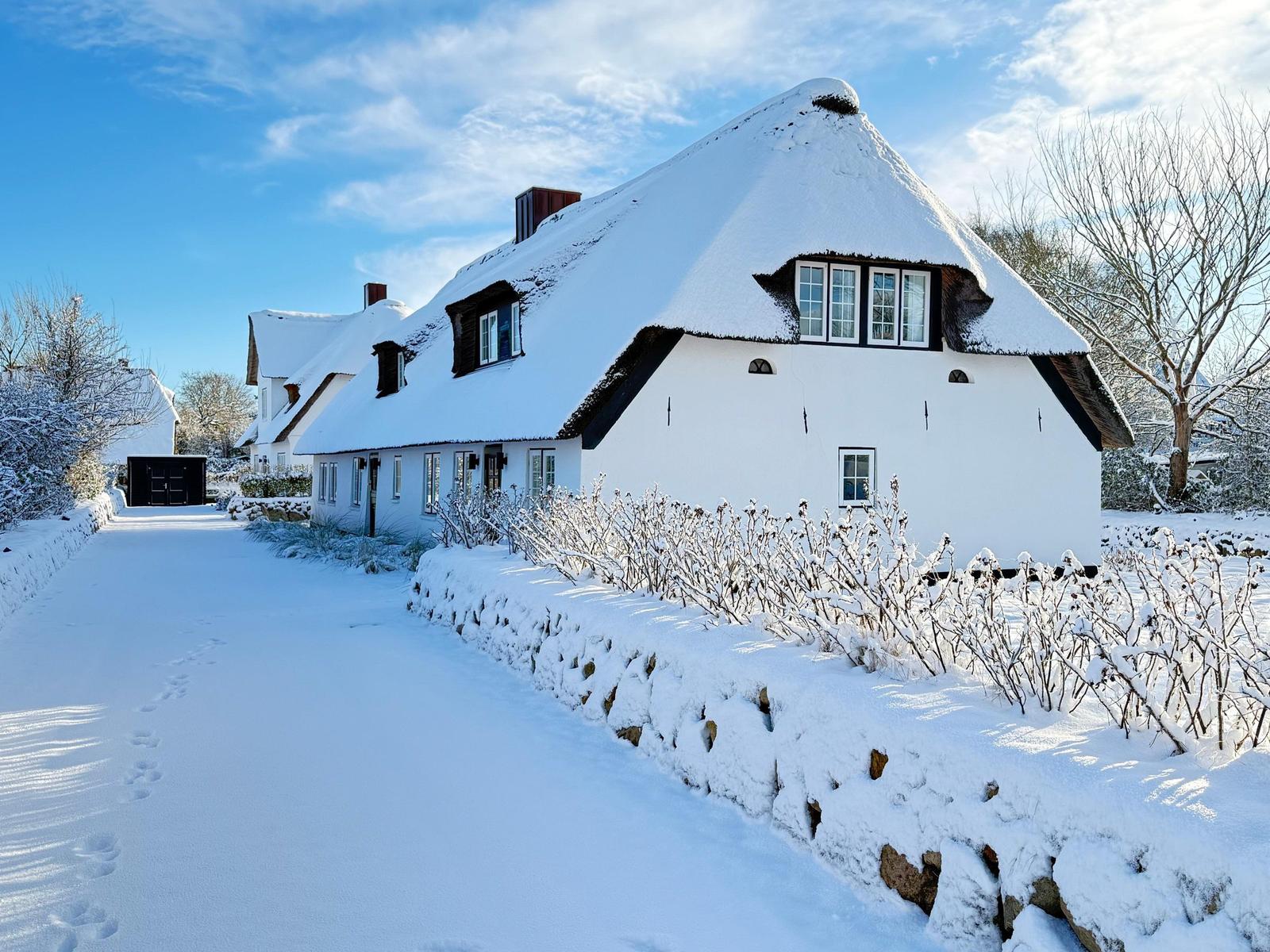 Schneebedecktes Haus mit strohgedecktem Dach und weißen Wänden.