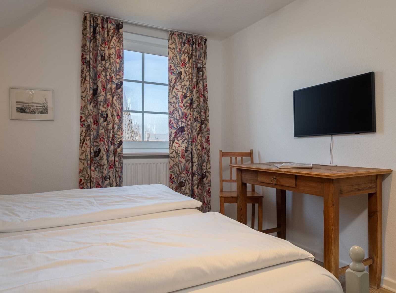 Schlafzimmer mit Bett, Sessel und Nachttisch unter schrägem Dach.