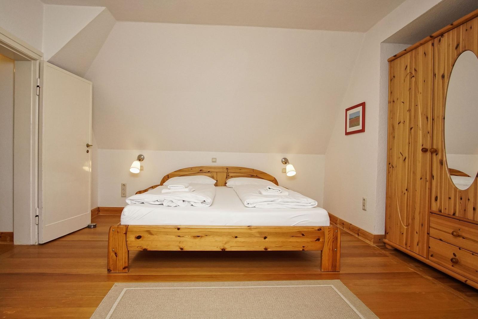 Schlafzimmer mit Holzbett, Kleiderschrank und Fenster mit Vorhängen.