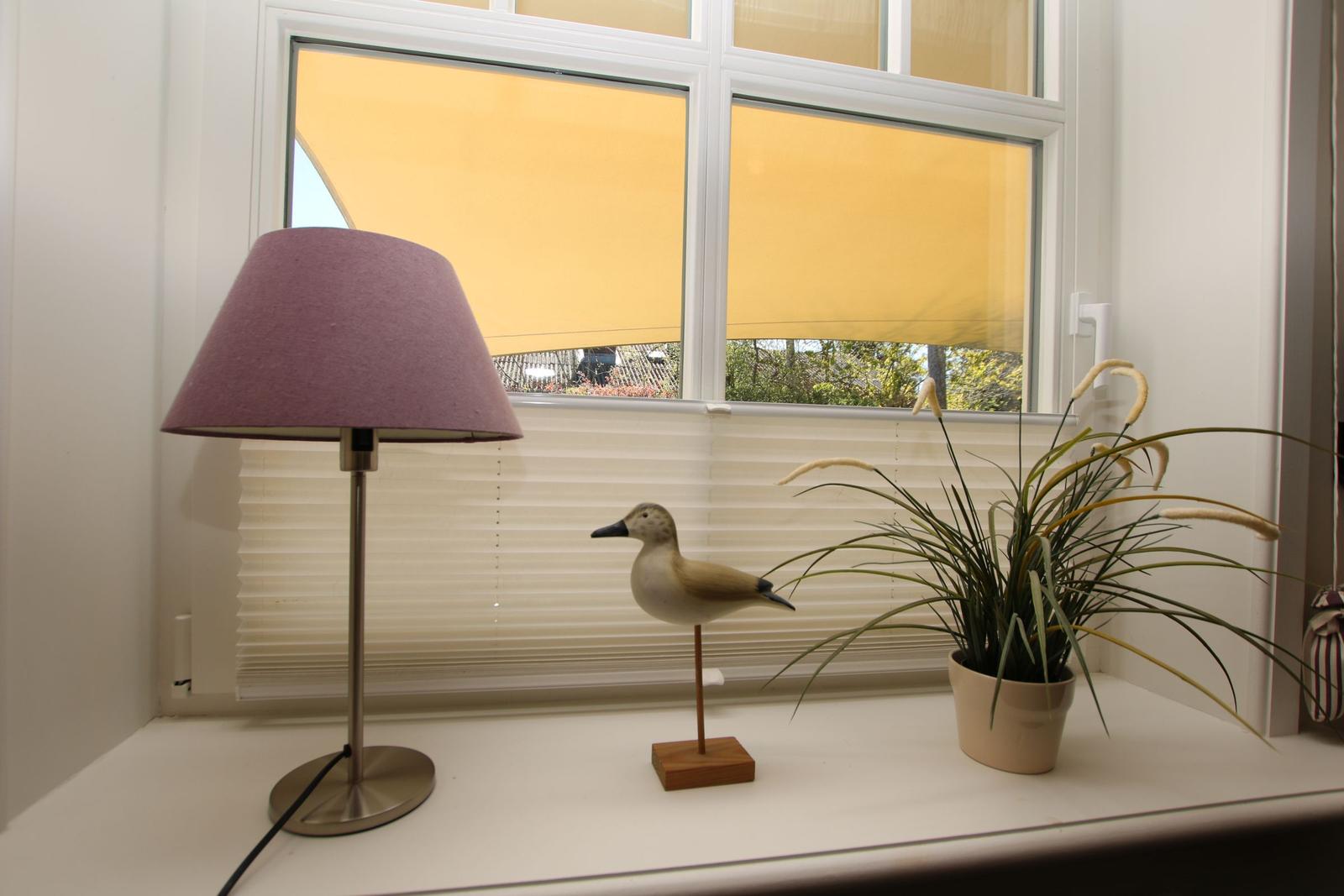 Fensterbalkon mit Tisch, Stühlen und Gläsern. Informationsblatt und Laterne auf dem Sims.