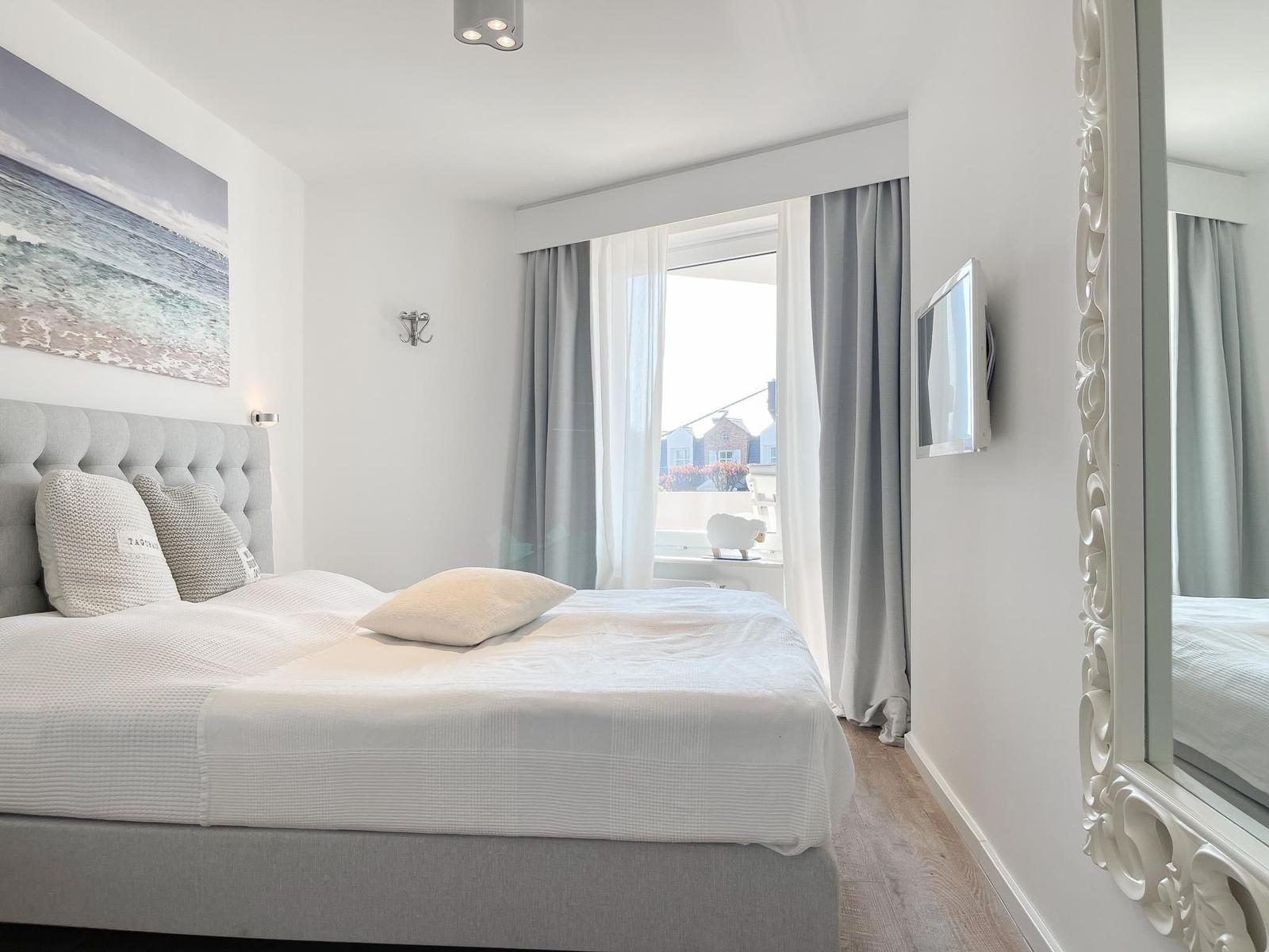 Schlafzimmer mit großem Bett, Wandbild und Fenster mit Blick.