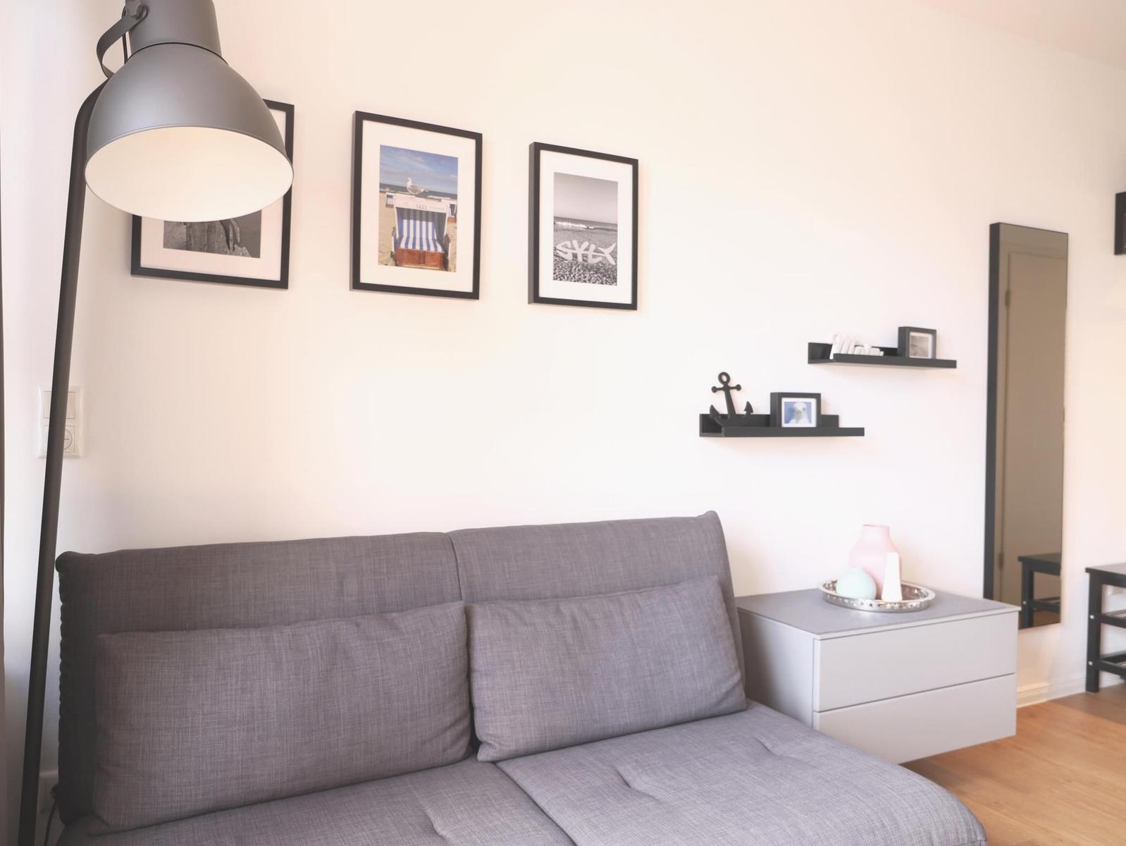 Graße Couch mit Kissen, Wandbilder und Nachttisch mit Deko.