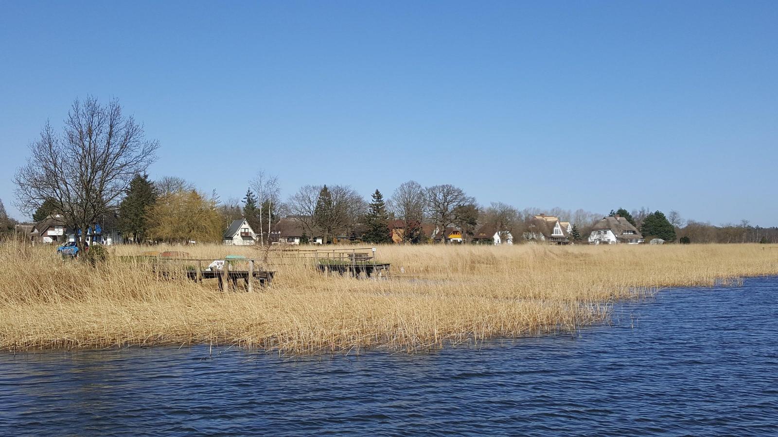 Drei Hütten am Wasser mit Spiegelungen und Booten im Herbst.