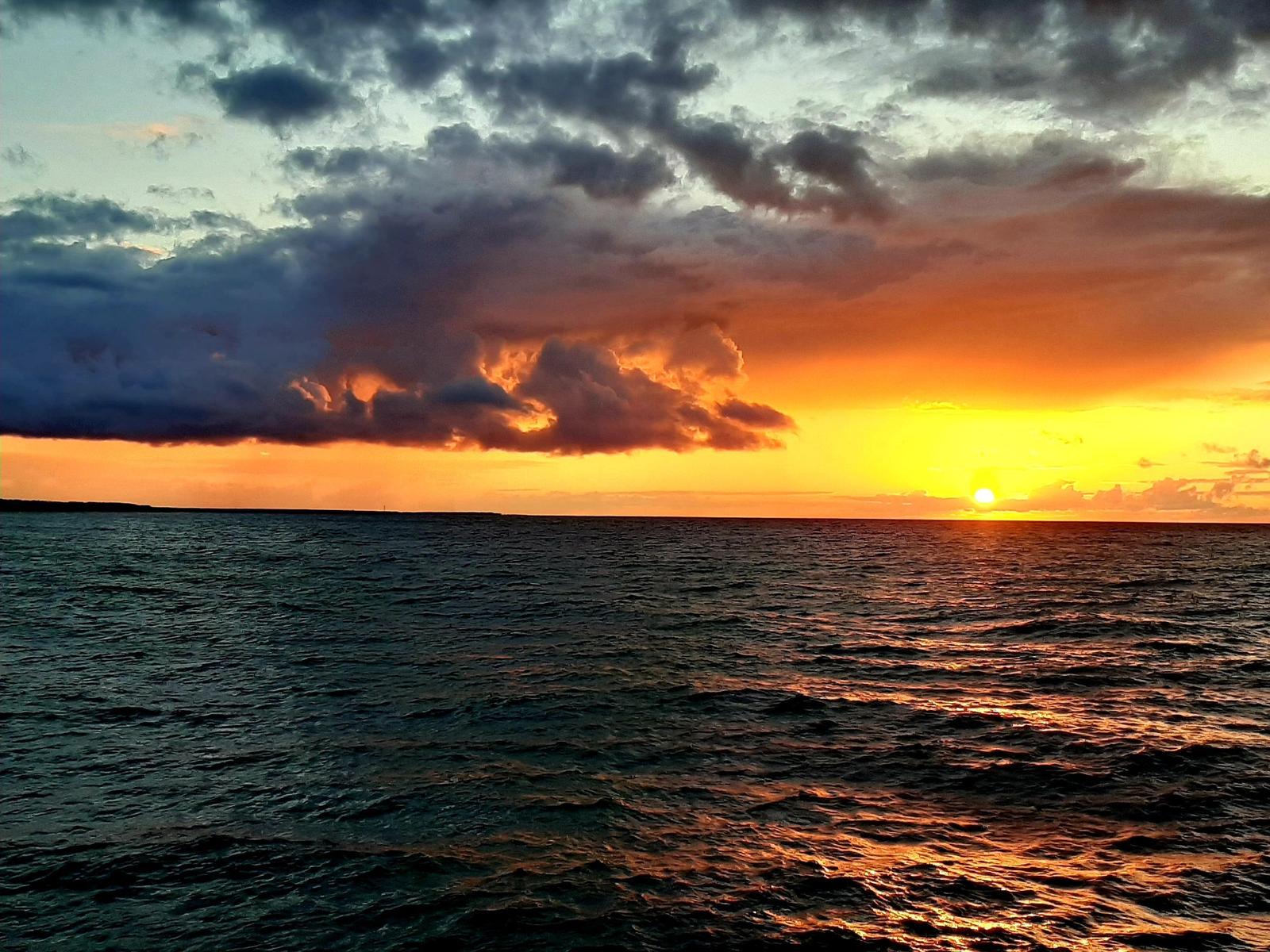 Sonnenuntergang über einem See mit goldenen Wolken und Uferlinie.