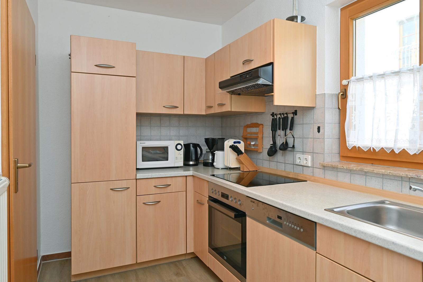 Küche mit Holzschränken, Induktionskochfeld und Spüle unter Fenster.