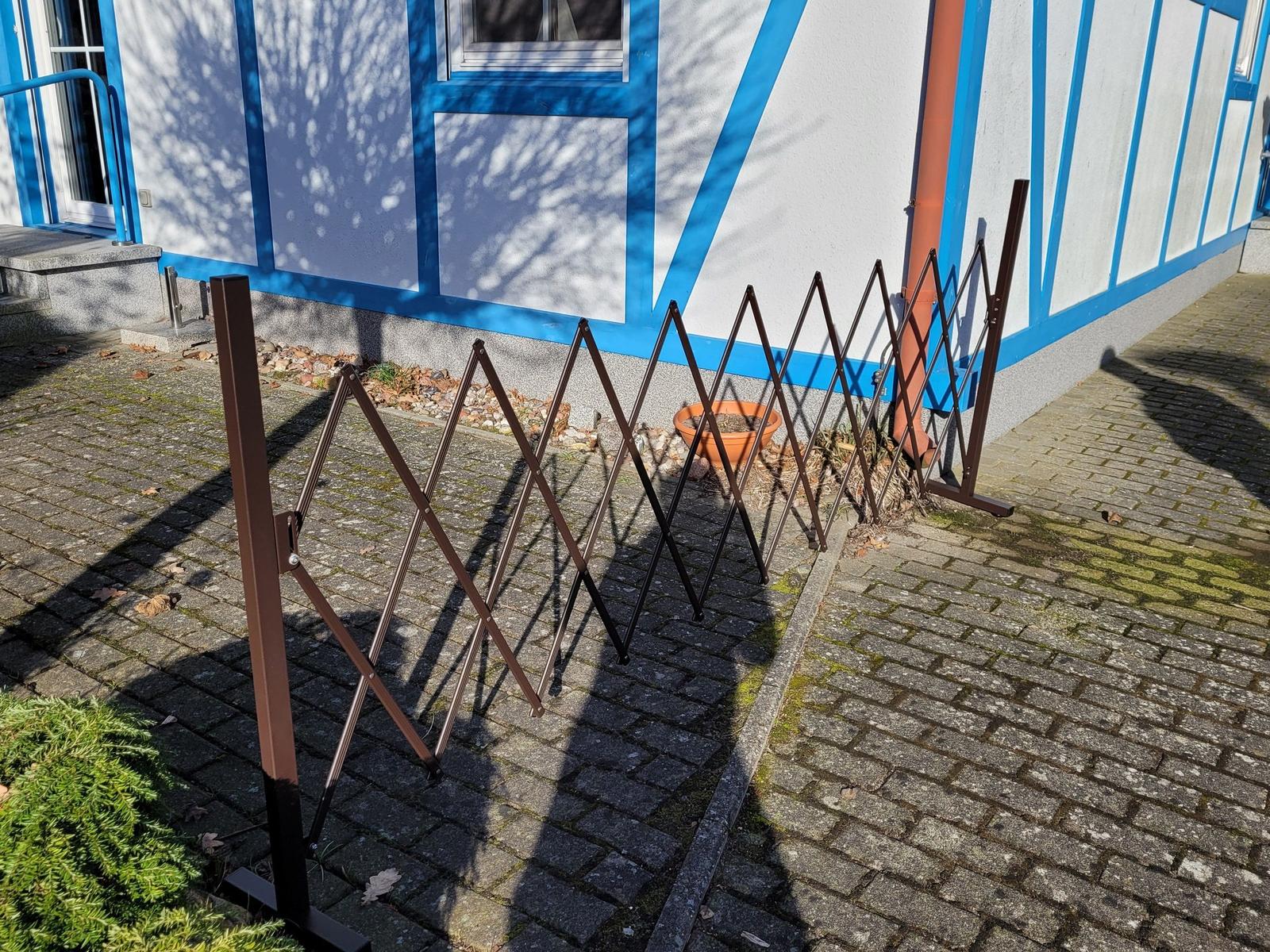 Einfacher, dunkler Metallzufahrtstore mit elastischem Gitterdesign steht vor einer Wand.