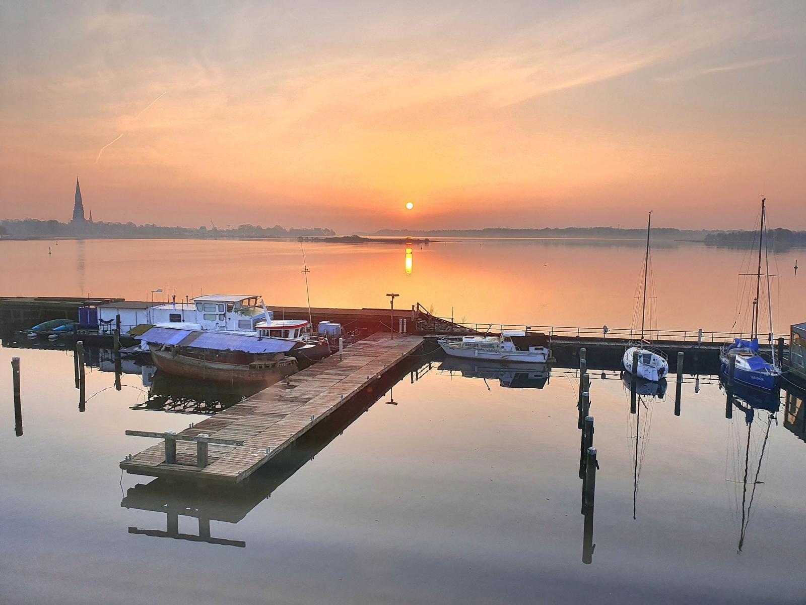 Sonnenuntergang über Hafen mit Booten und Docks. Im Hintergrund ist ein Turm sichtbar.