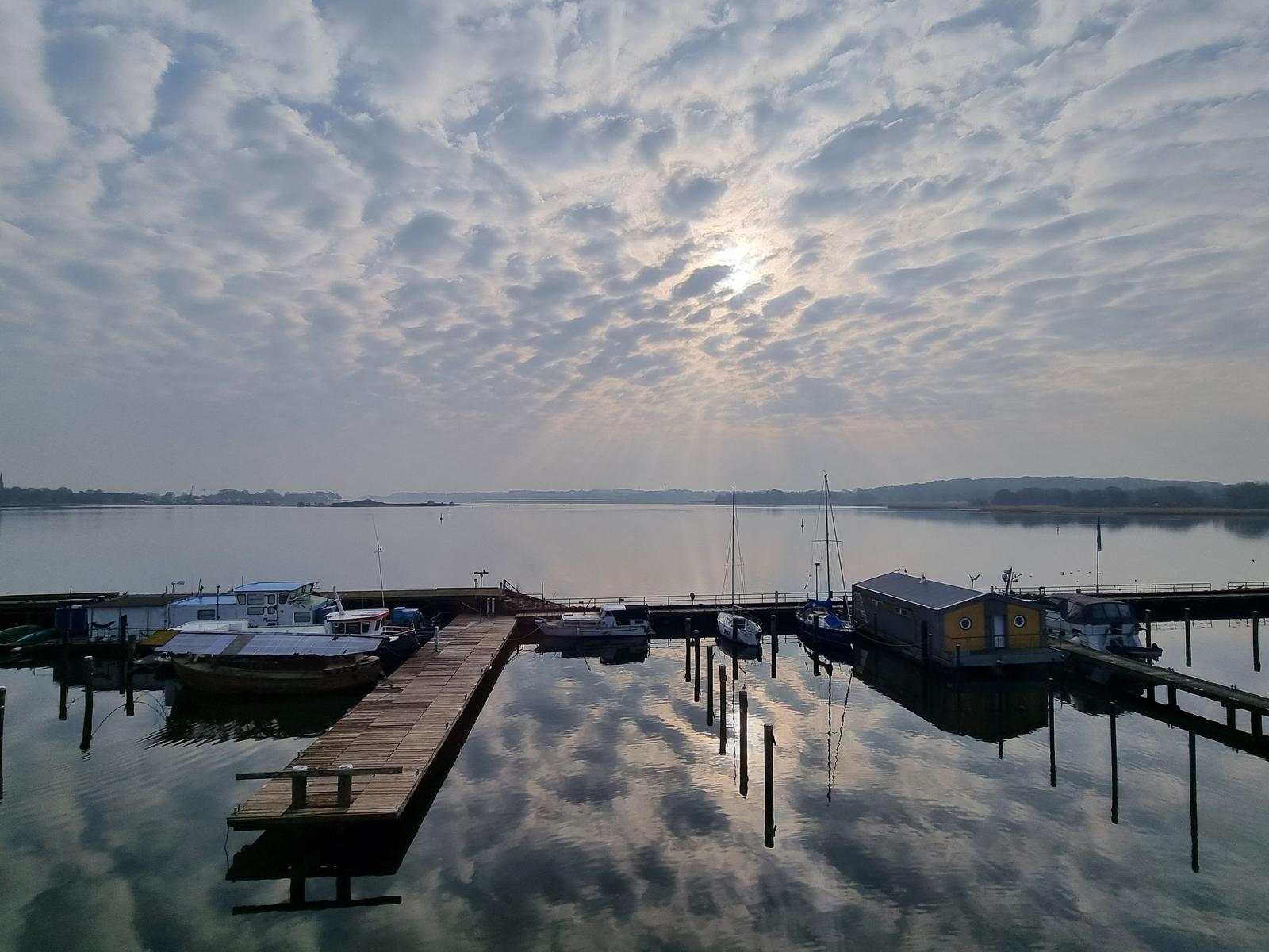 Sonnenuntergang über Hafen mit Segelyacht und Kirchturm im Hintergrund.