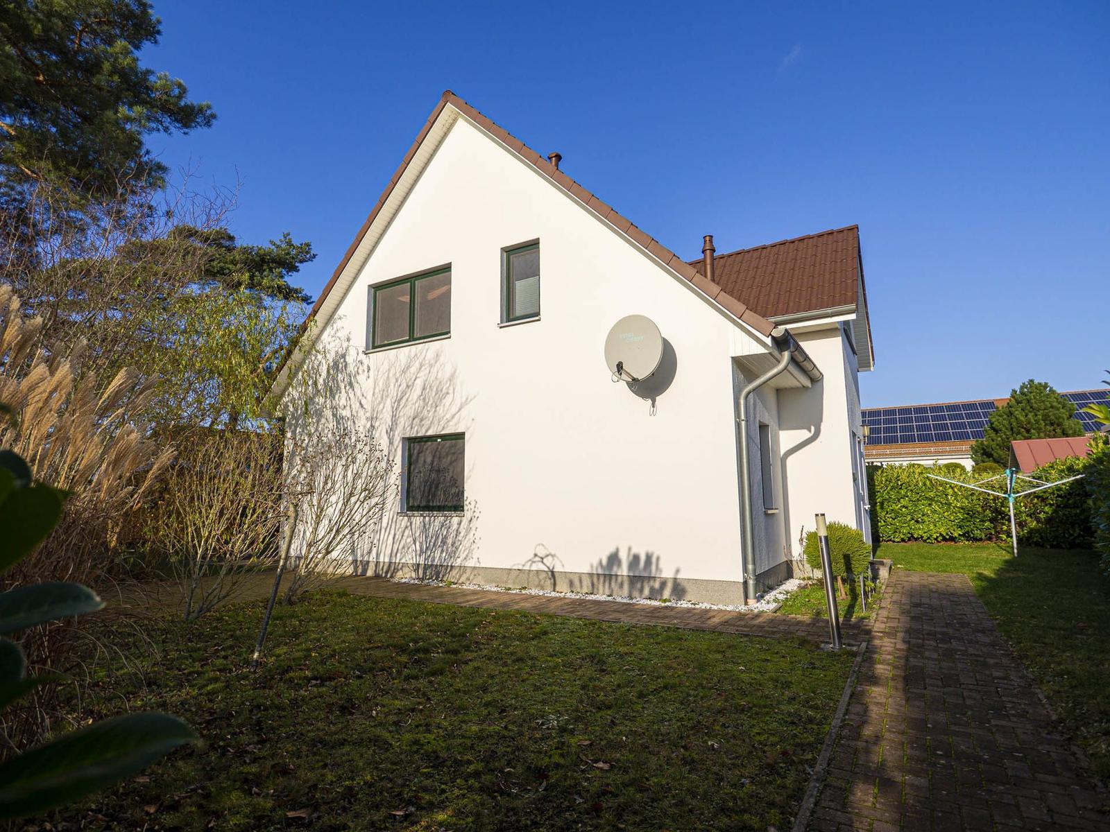 Hinterhof mit Holzschuppen, Spielgeräten und Bäumen. Grasfläche und gepflasterter Weg.
