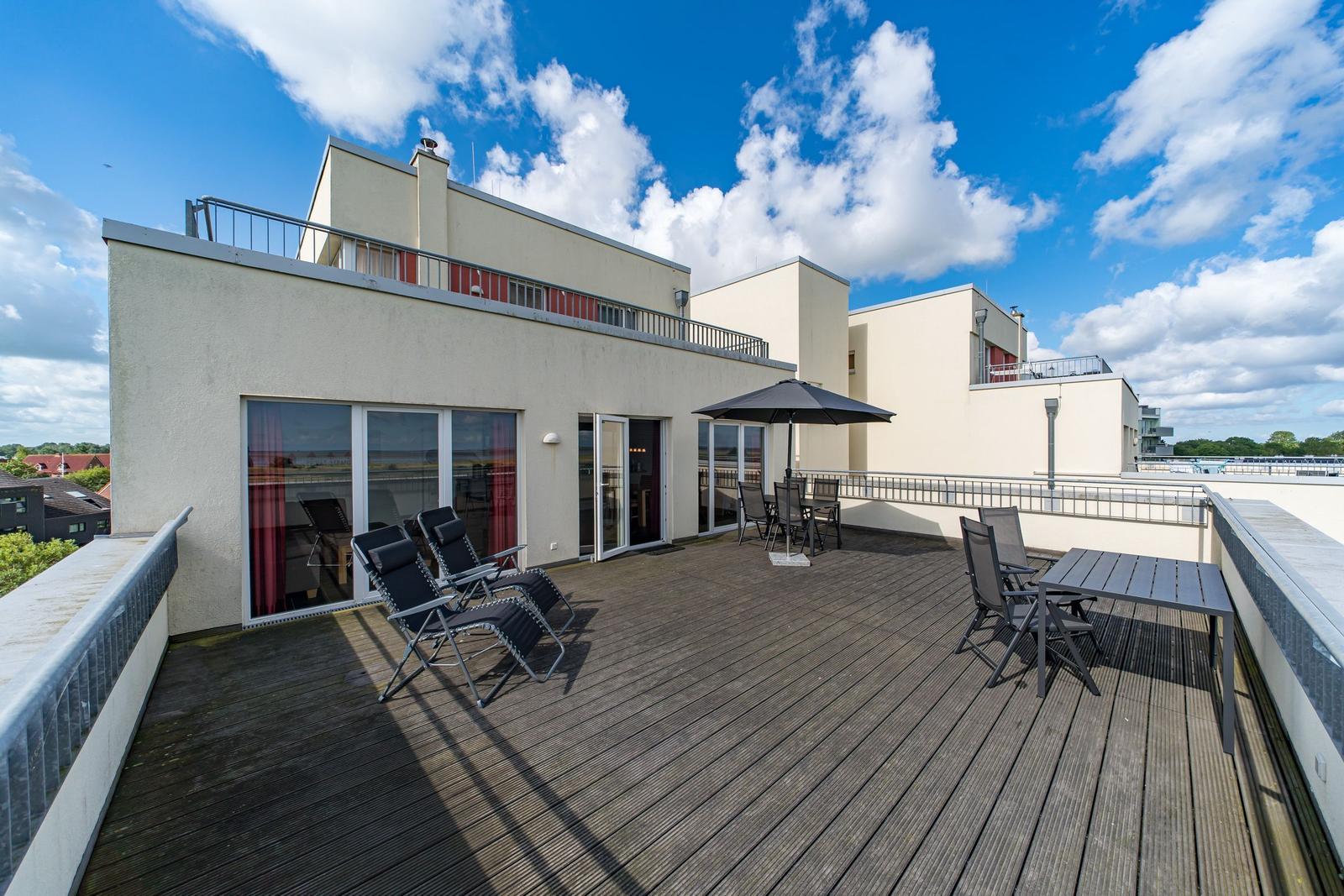 Terrasse mit Sonnenschirm und Gartenmöbeln. Blick auf Fluss und Himmel.