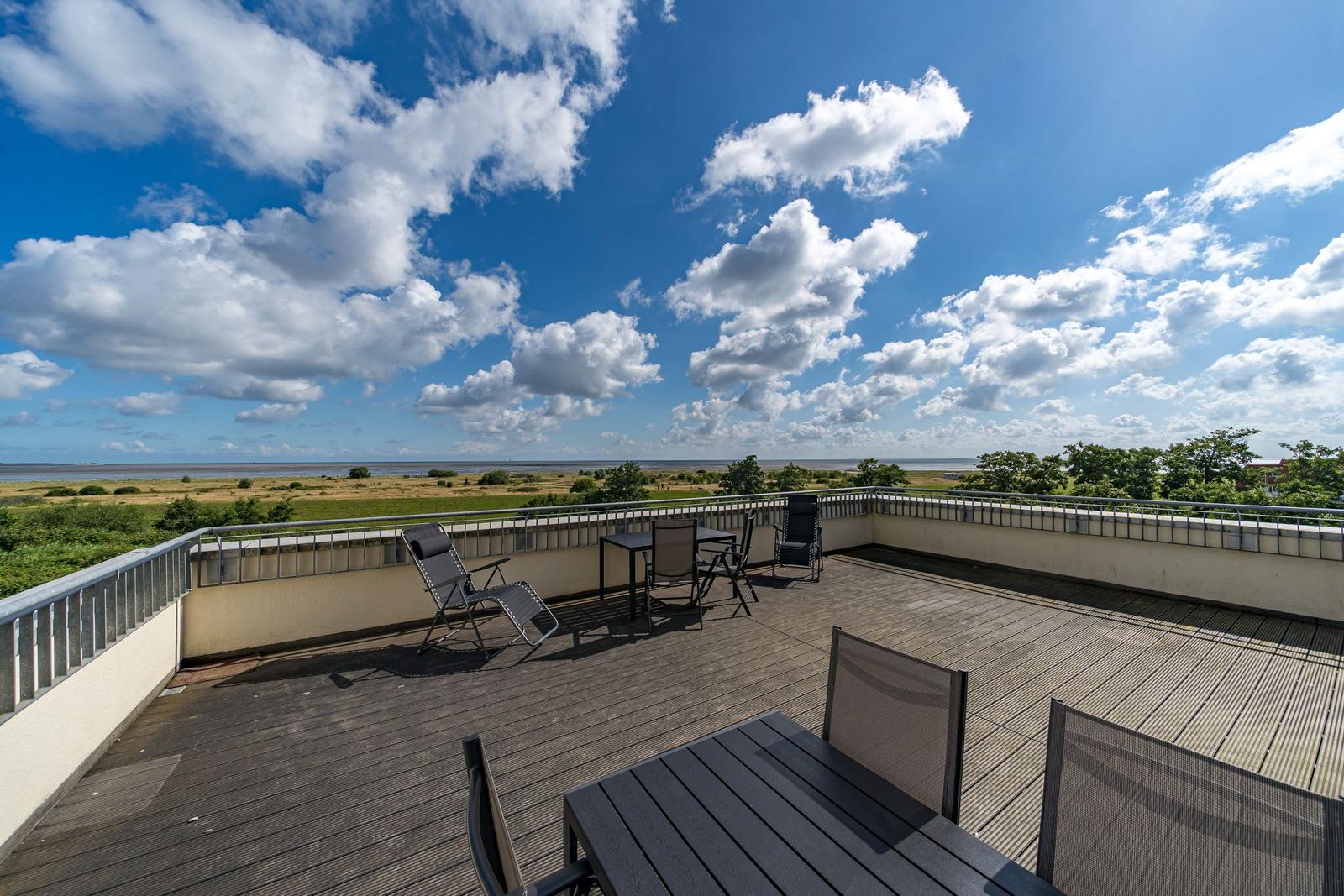 Weitläufiger Blick auf Fluss, Grünflächen und Horizont unter blauem Himmel mit weißen Wolken.