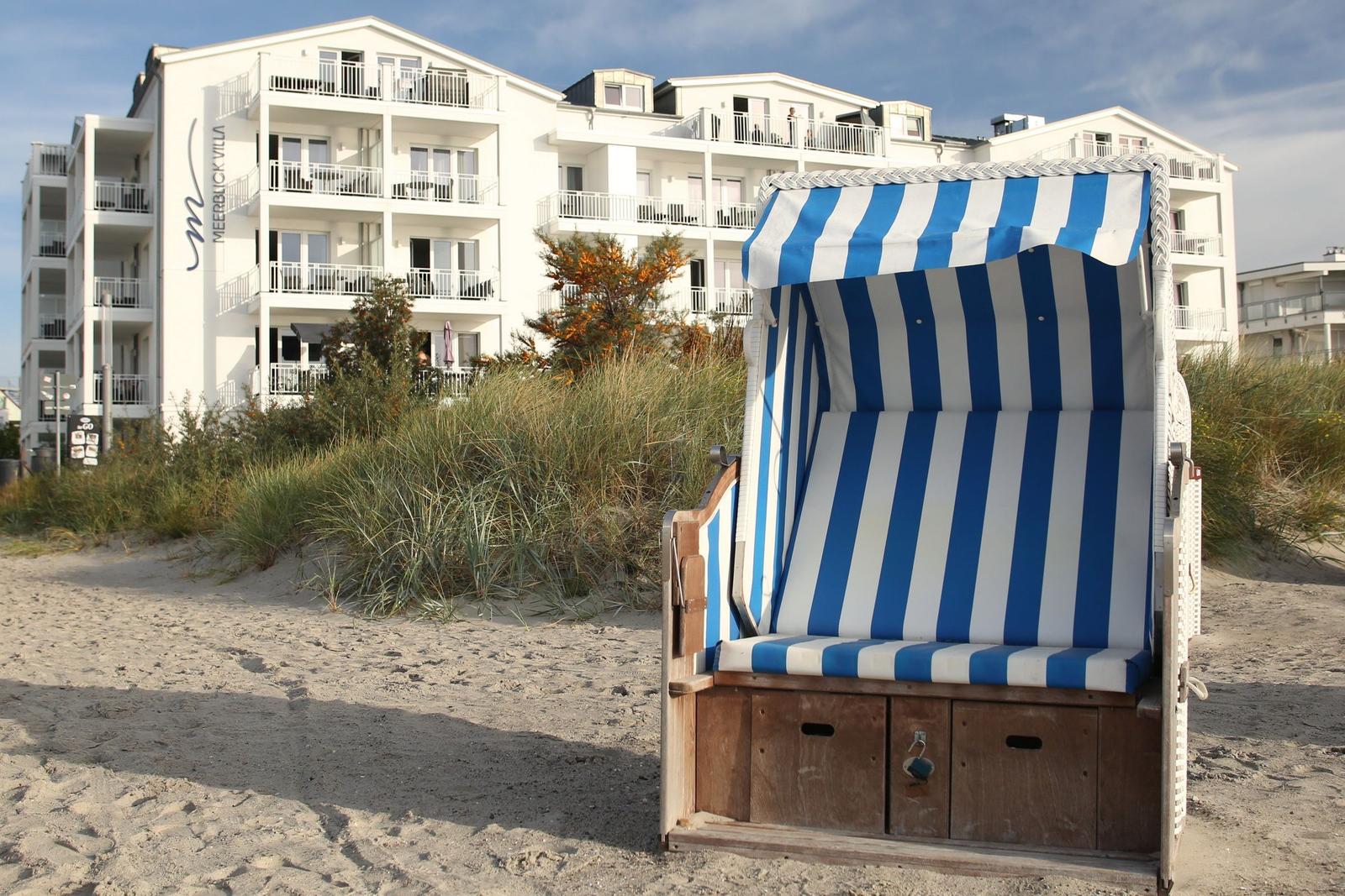 Weißer Strandkorb mit der Nummer 54-22 steht am sandigen Ufer.