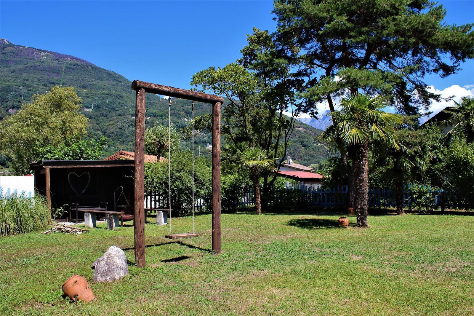Holzhaus mit Terrasse, Palmen und Bergblick. Weiße Garage mit Kfz.