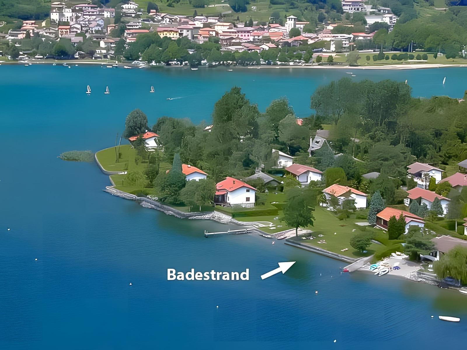 Strand mit Windsurfbrett und Segel, Menschen genießen das Wasser und die Berge.