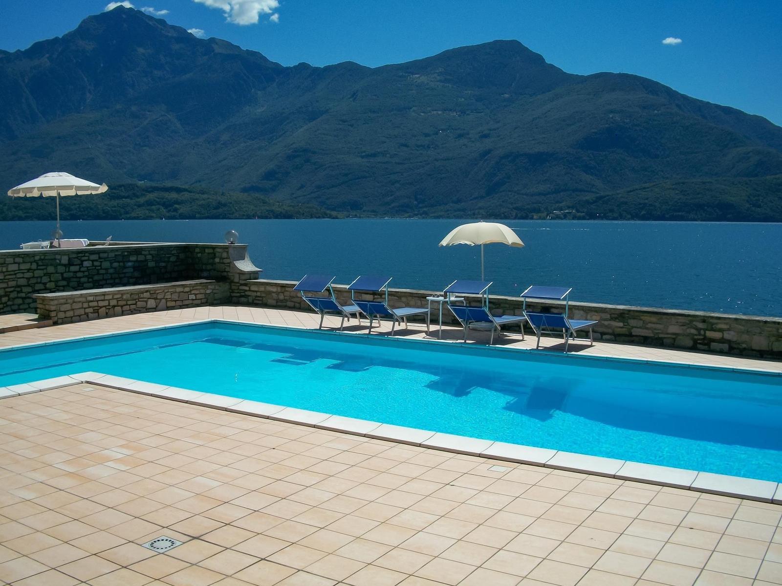 Terrasse mit Liegestühlen und Sonnenschirmen am See. Hintergrund: Berg und Wasser.