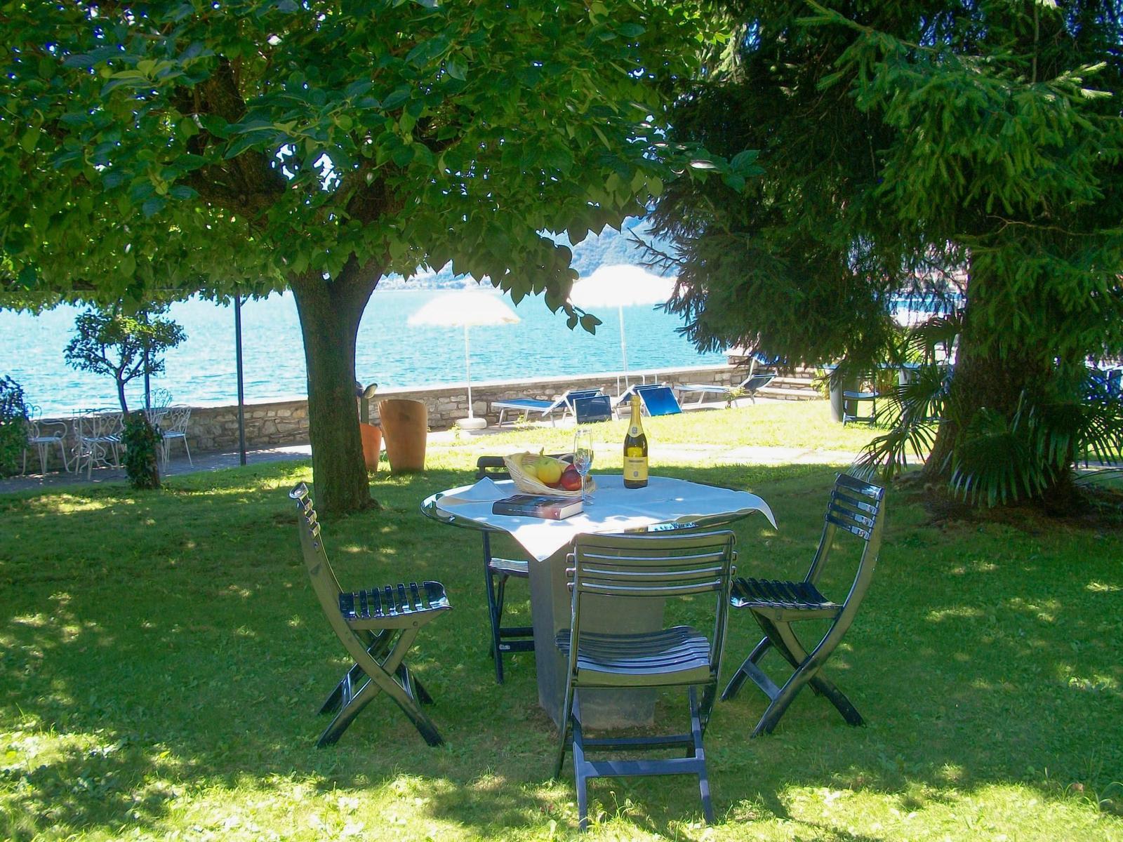Garten mit Tisch und Stühlen, Blick auf See und Berge. Pool und Terrasse im Hintergrund.
