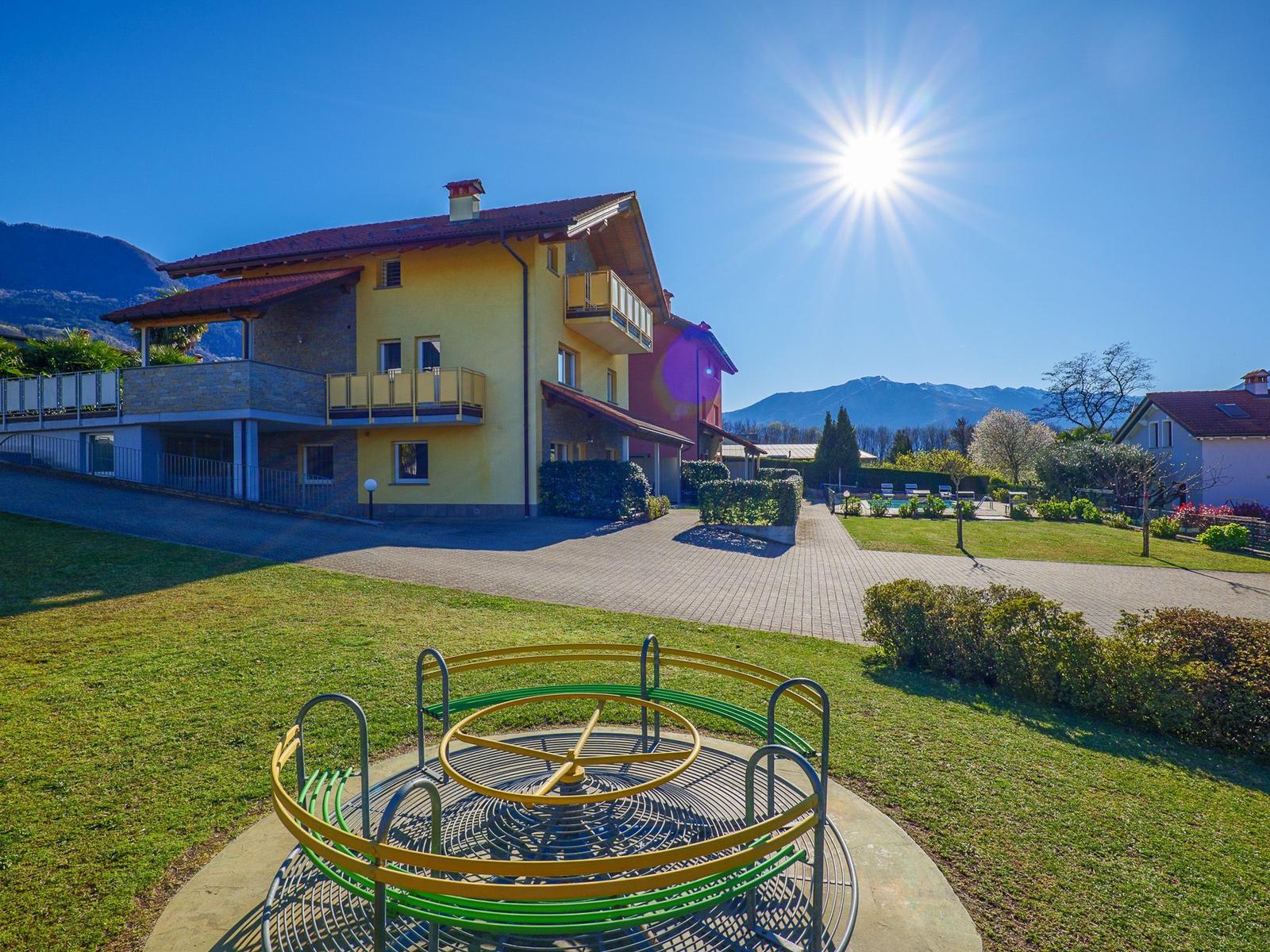 Green garden with childrens playground and ping pong table against mountain backdrop.