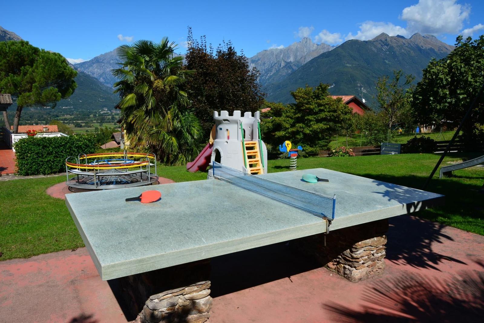 Großer Garten mit Spielplatz, Sandkasten und Schaukel. Hintergrund: Haus und Berge.