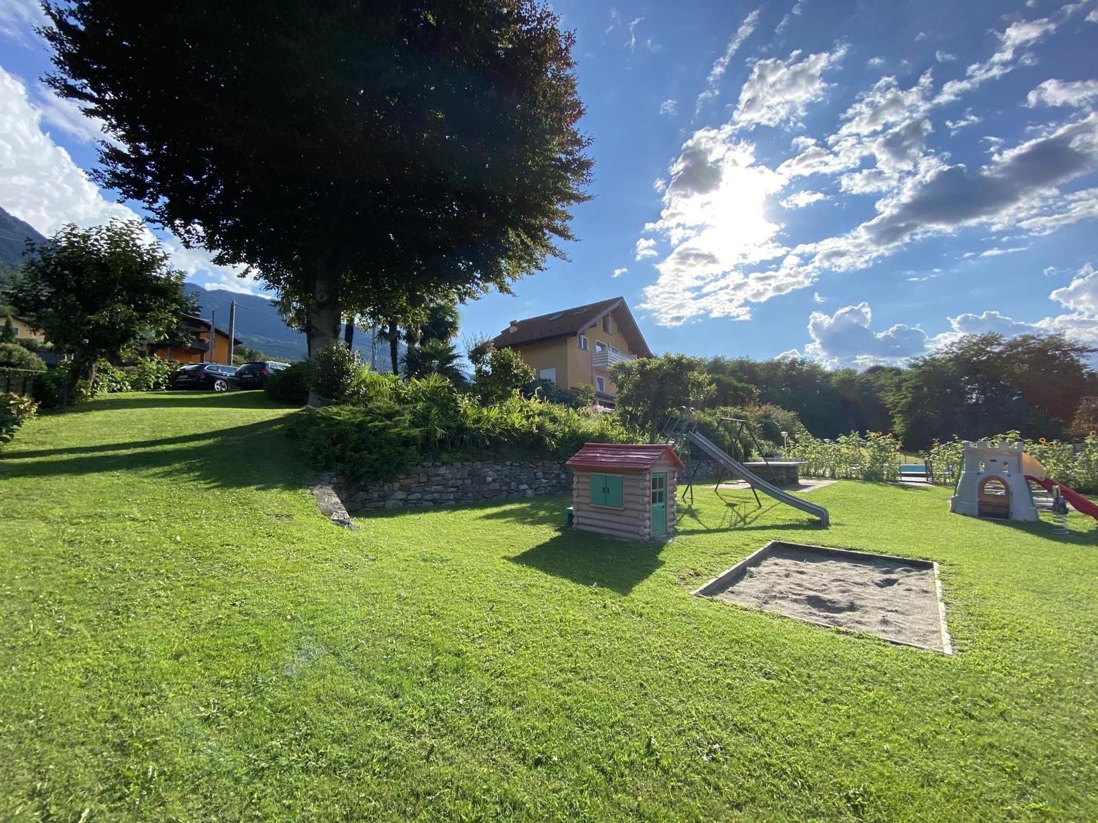 Wasserfall fließt über Felsen in einen Fluss mit Steinen und grüner Vegetation im Hintergrund.